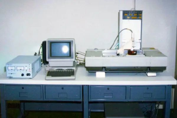 Una de las primeras impresoras 3D comerciales sobre una mesa junto a una computadora de los ochenta