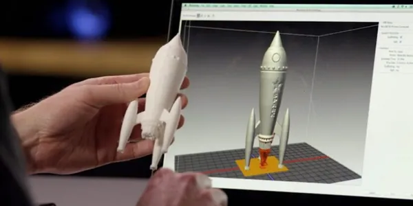 Prototipo impreso de un cohete sostenido frente a la pantalla con su modelo 3D en el software de laminado