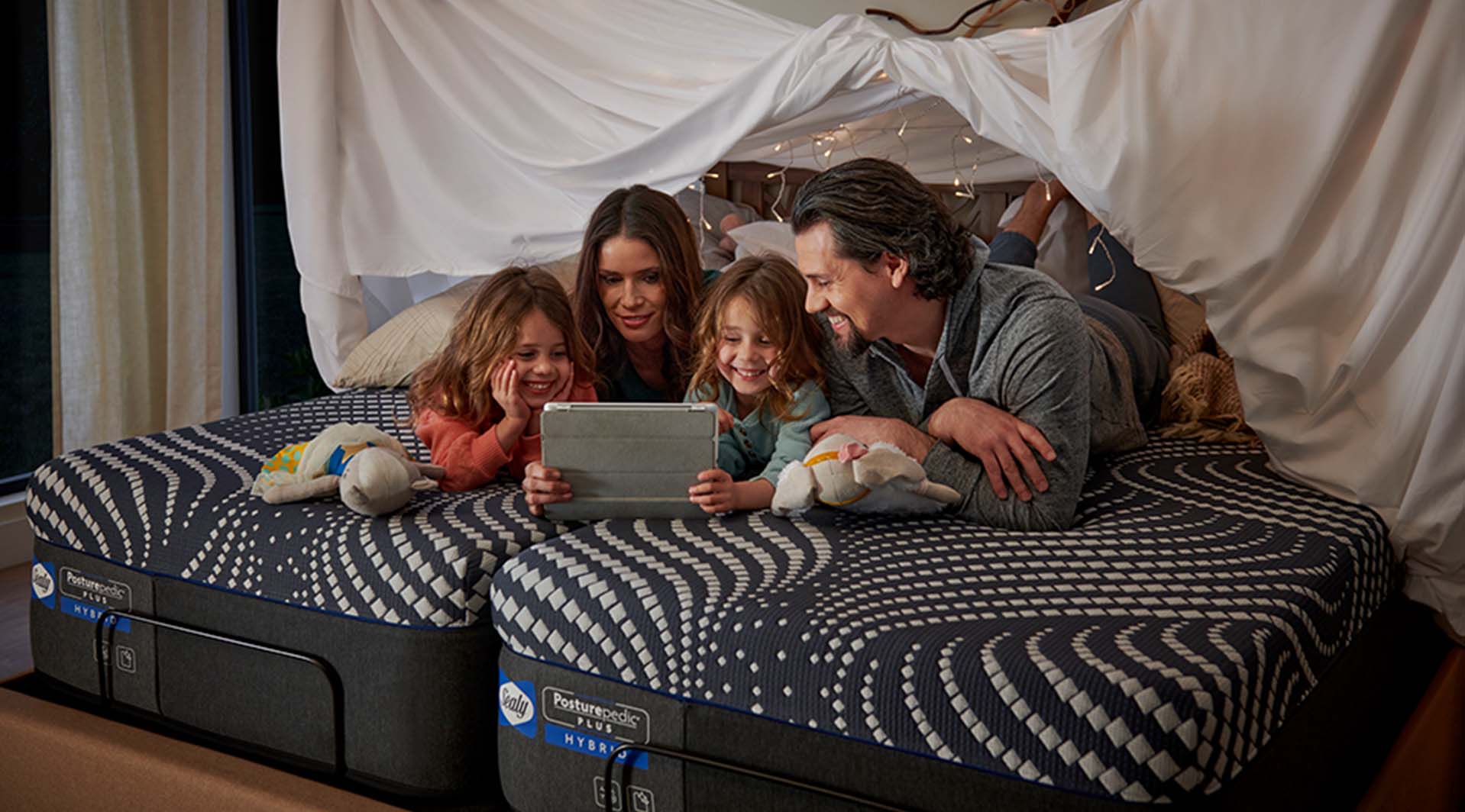 Family of four using tablet on Sealy® mattress