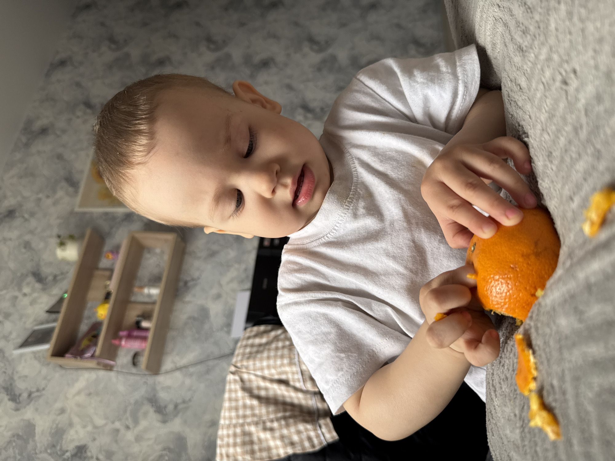 Child peels orange on sofa in Rusanovo morning scene