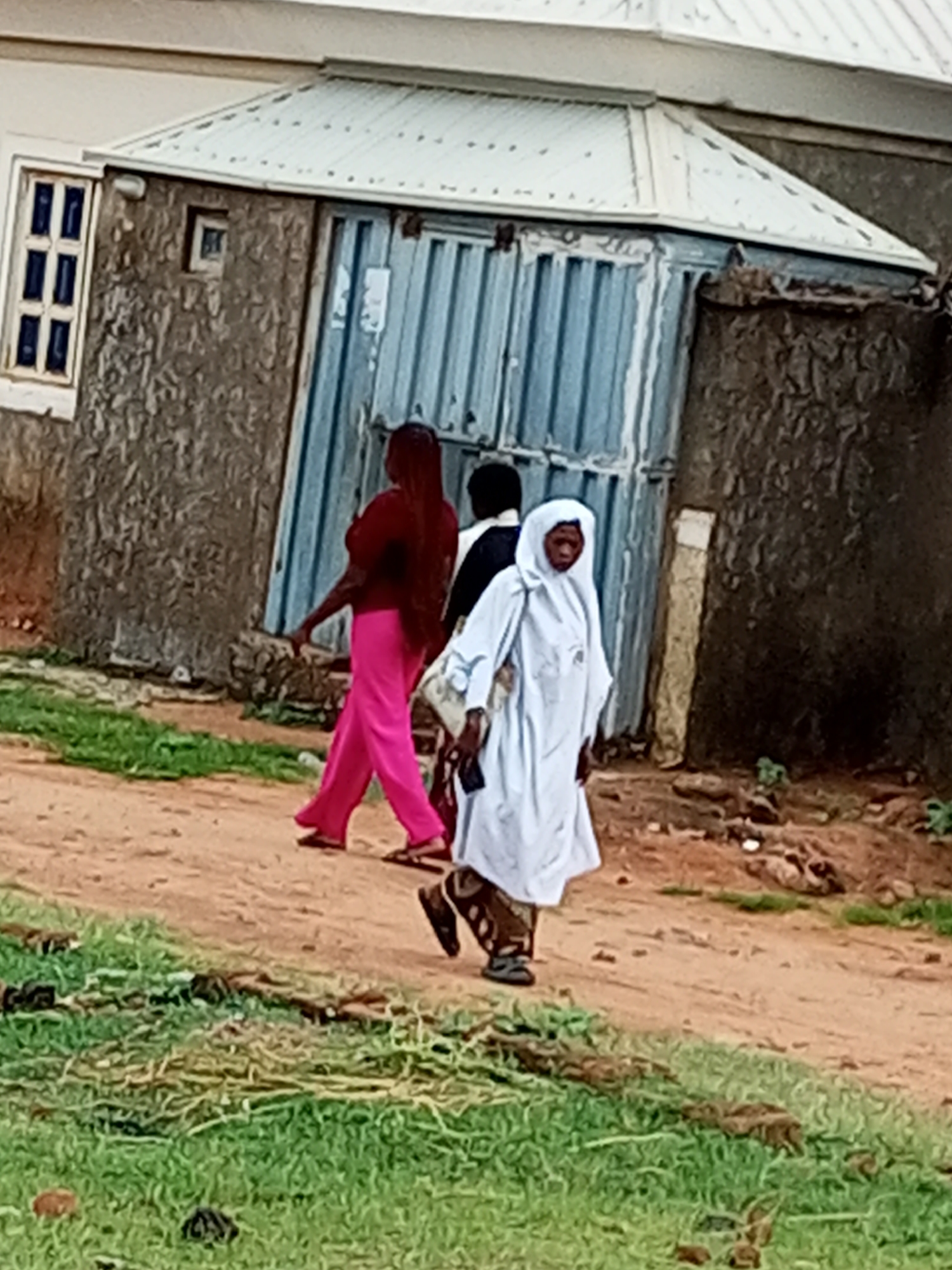 Quiet morning foot traffic on a dirt path in Tumfure, Nigeria