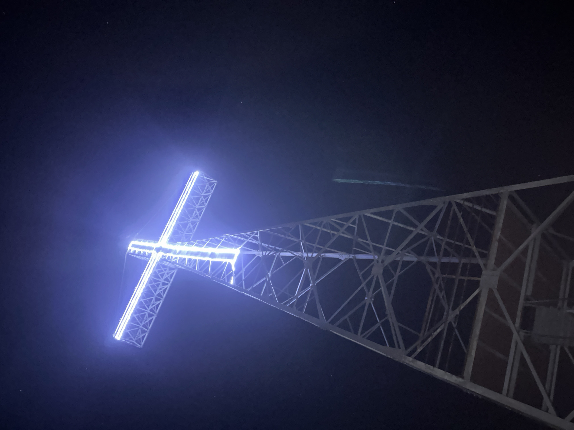 Blue-lit cross glows atop steel structure in nighttime observation