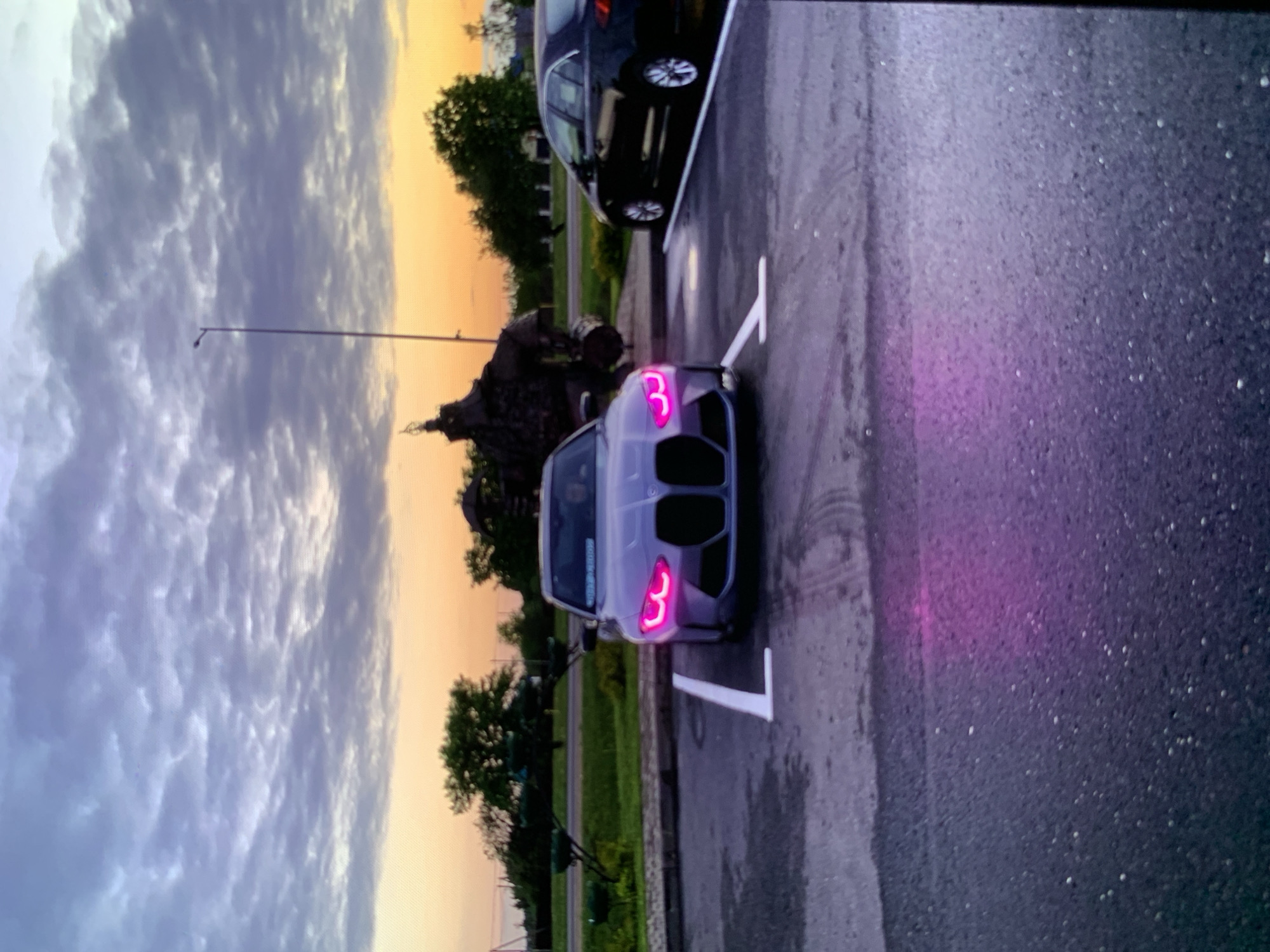 Gray BMW M3 parked at dusk with glowing pink headlights