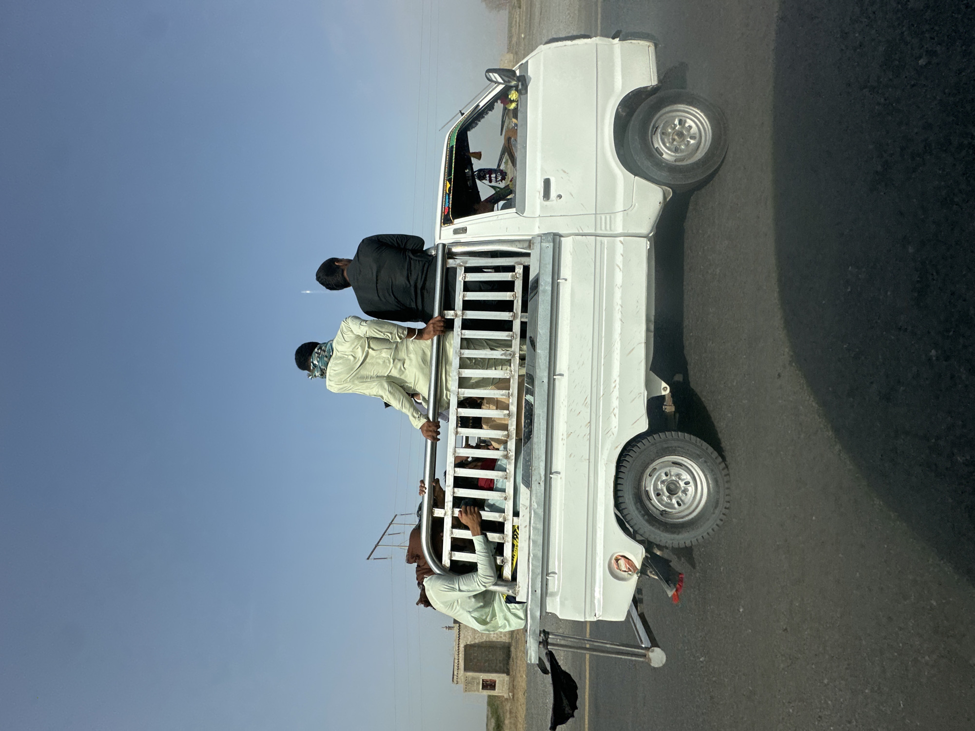 White pickup truck carrying passengers along a Pakistani road