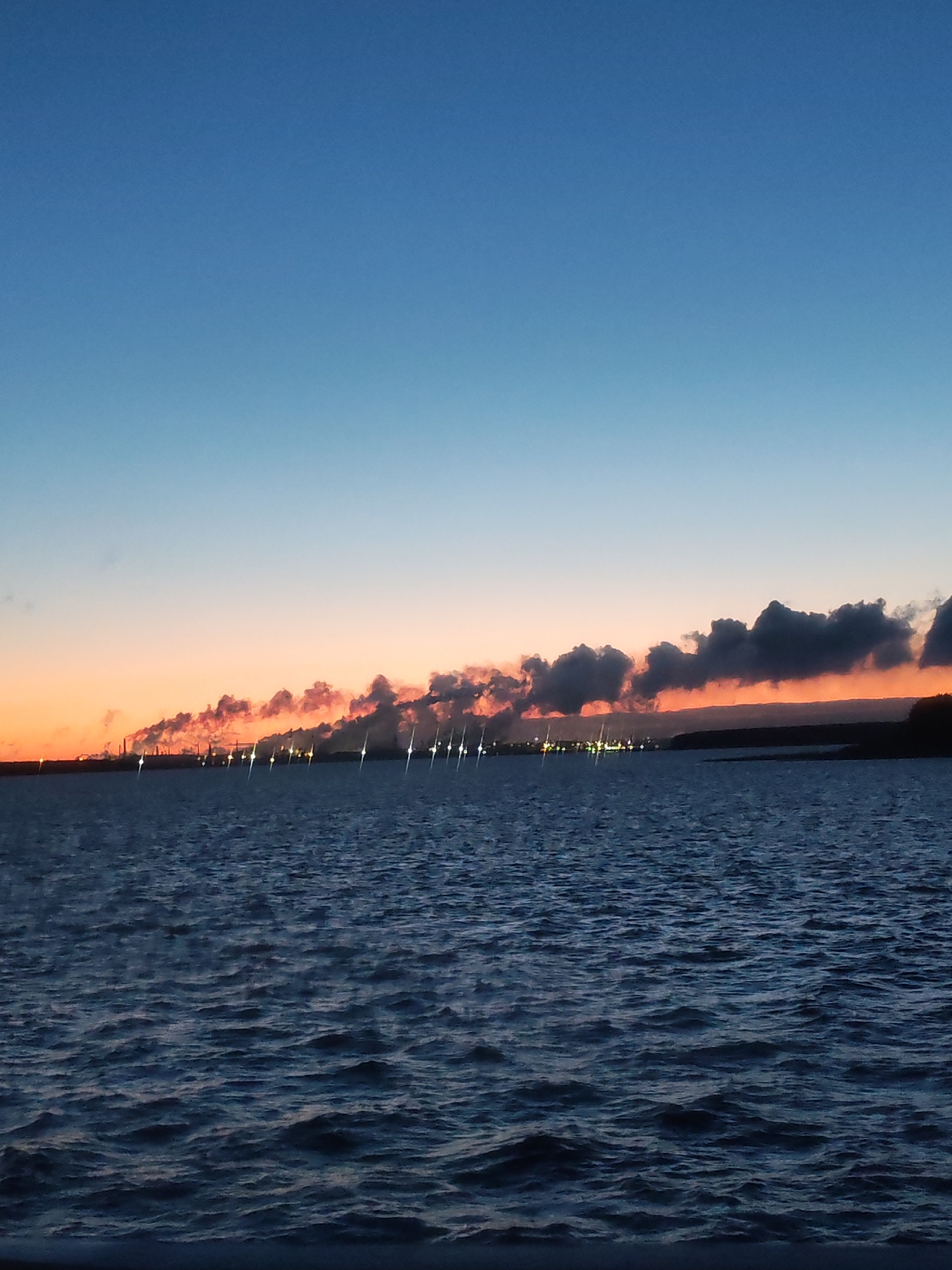 Industrial waterfront scene documented at dusk with illuminated vessels