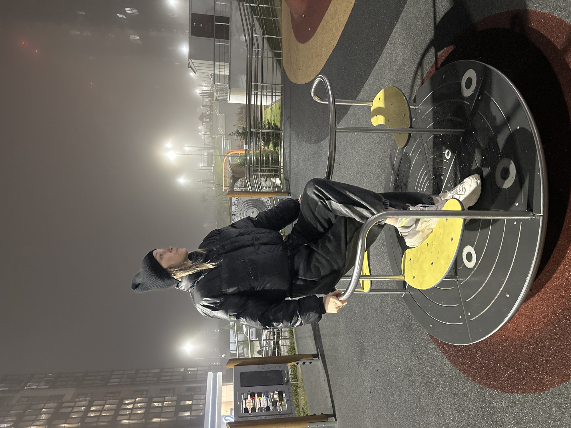 Person in black sits on playground merry-go-round at night