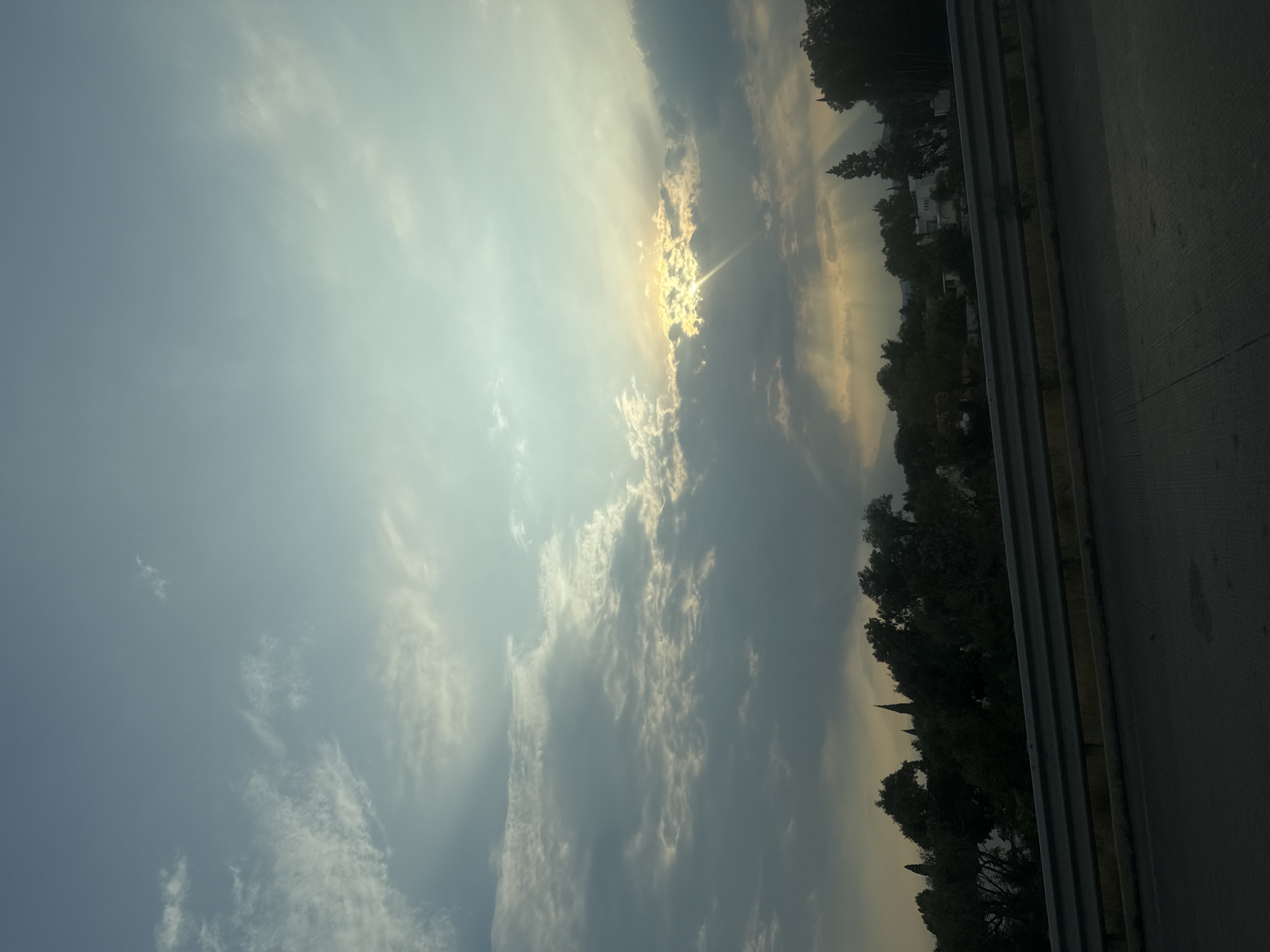 Cloudy skies with breaking sunlight observed over roadside area