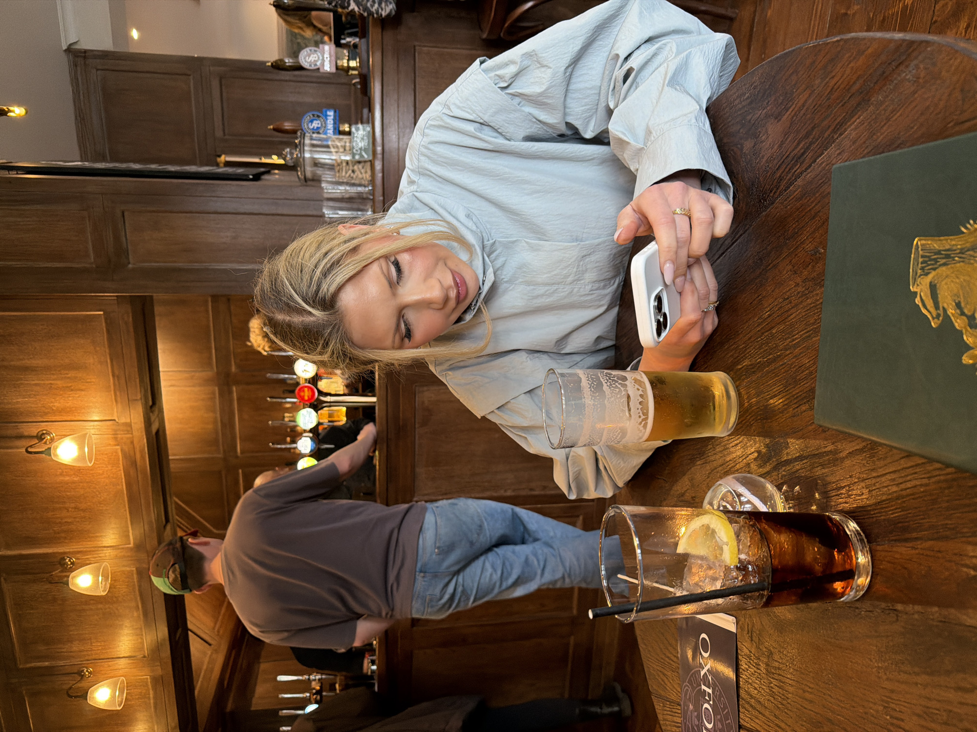 Woman uses phone at London pub table with drinks
