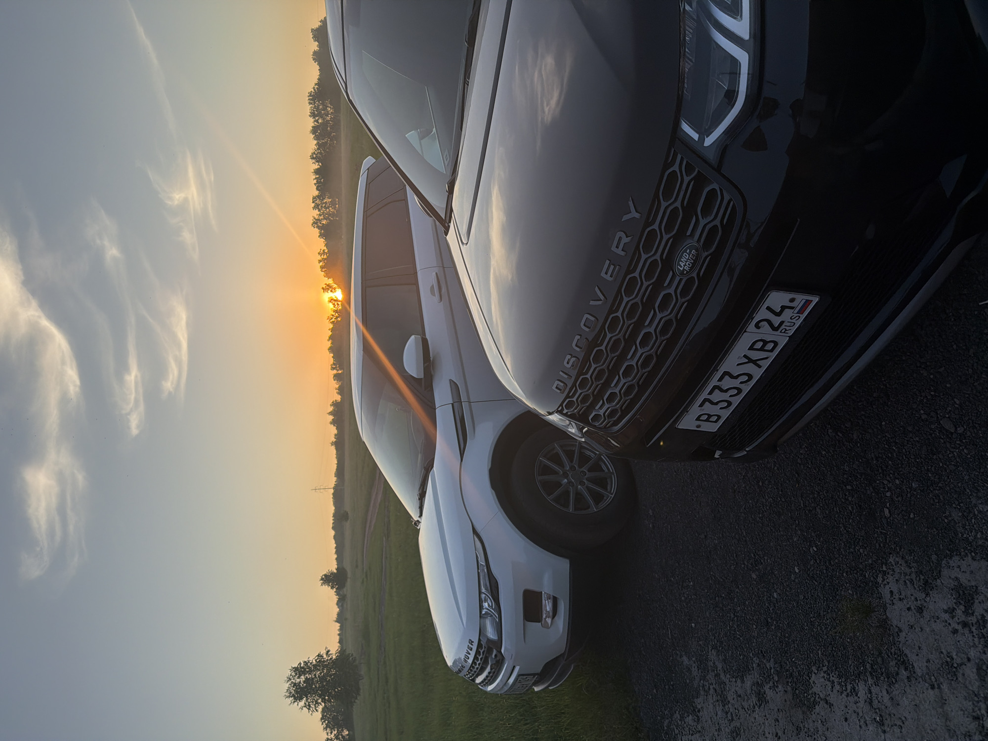 Two luxury SUVs parked in residential Krasnoyarsk during sunset