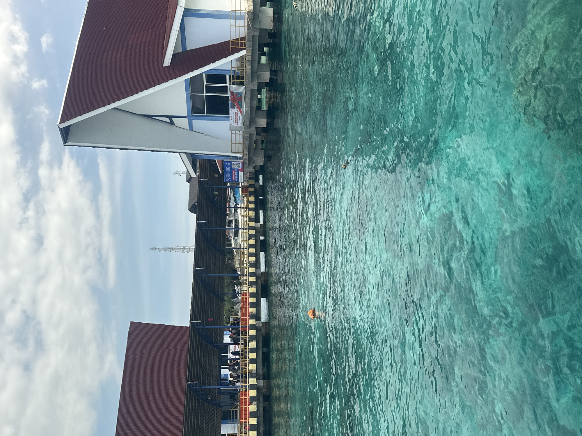 Boats navigate Indonesian waters near pier with mountainous backdrop