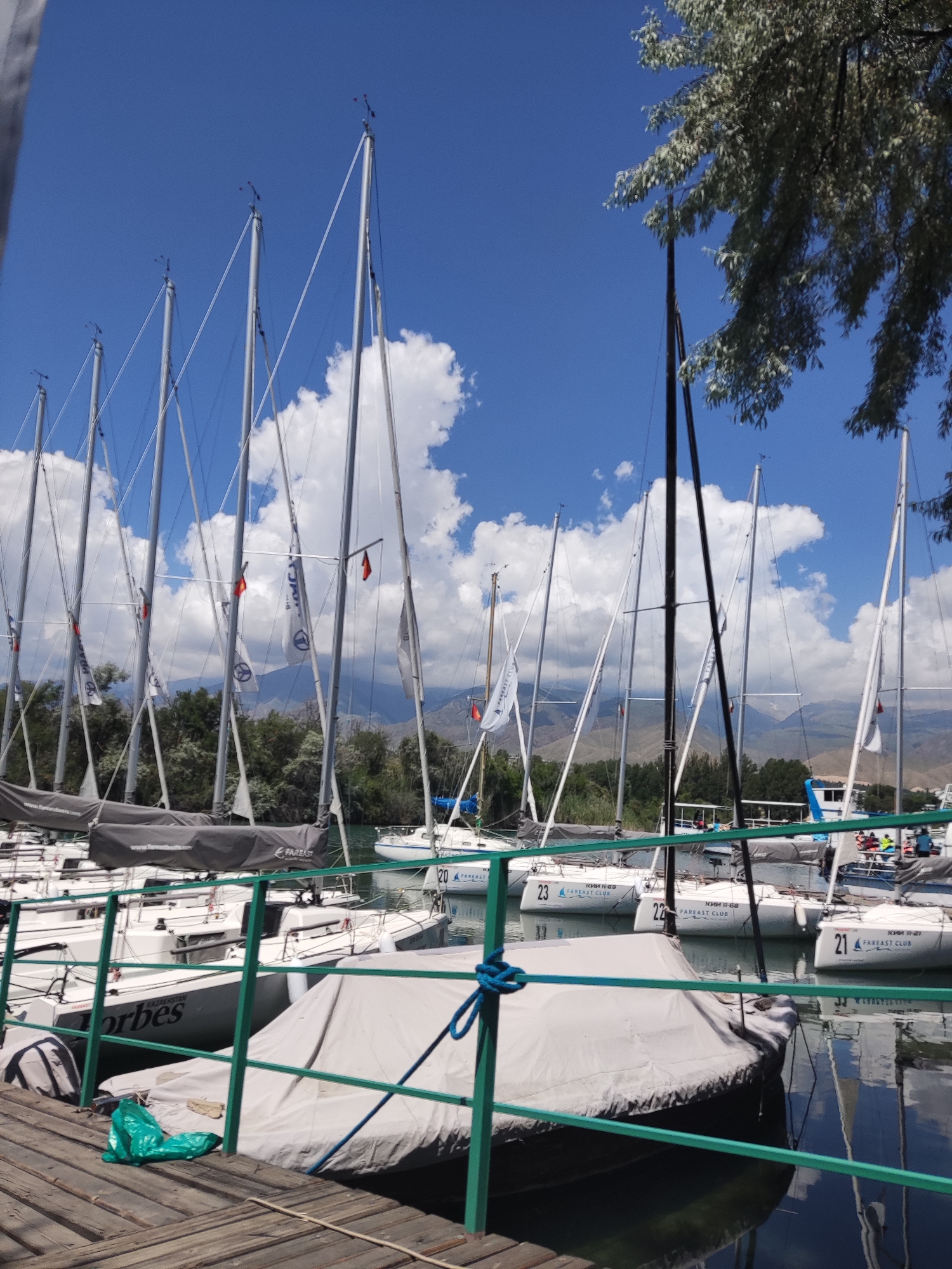 Sailboats and calm water at Cholpon-Ata's lakeside on a summer morning.