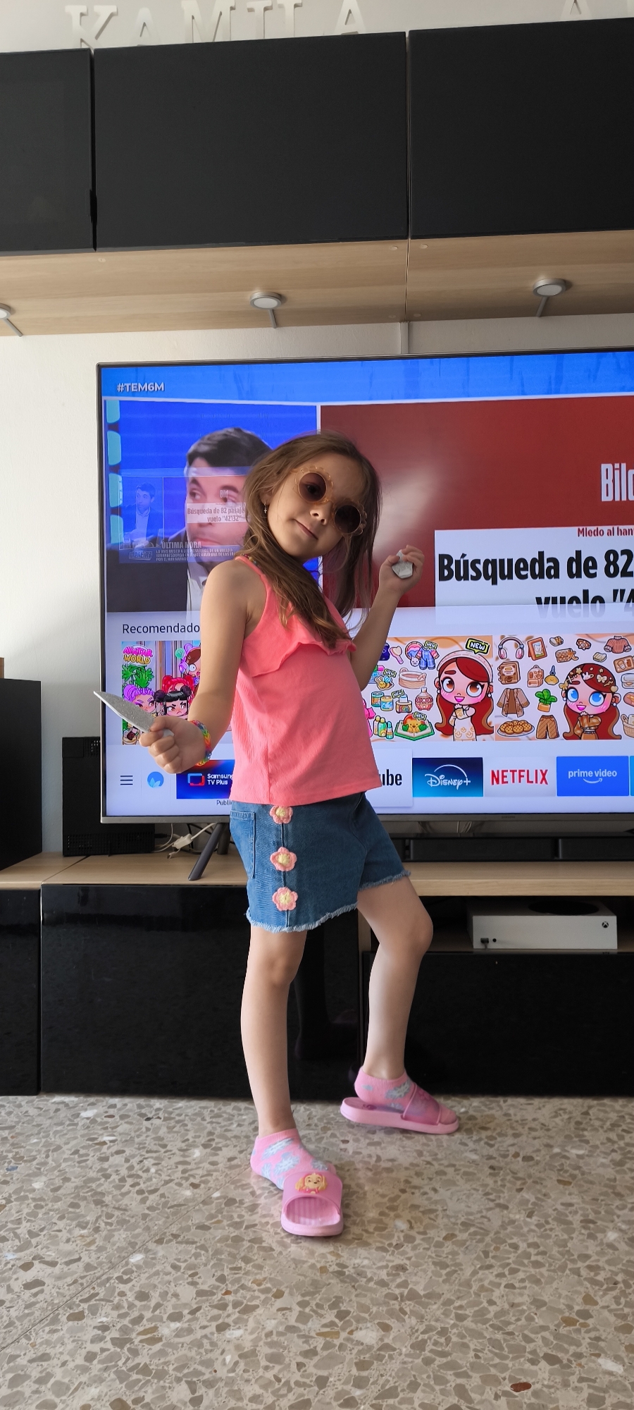 Girl in pink outfit and sunglasses stands by TV