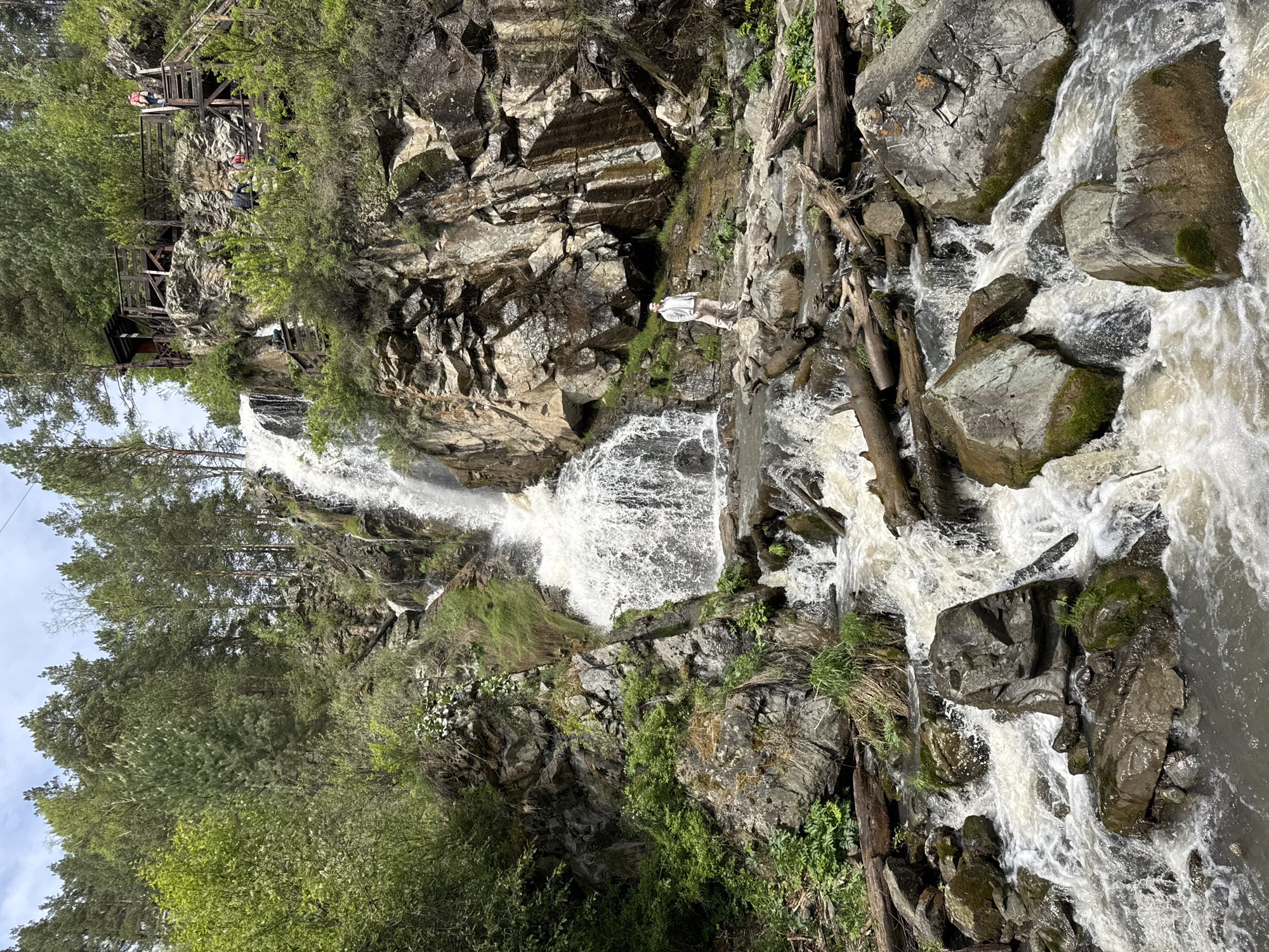 Person stands at waterfall amid lush vegetation in Barangol