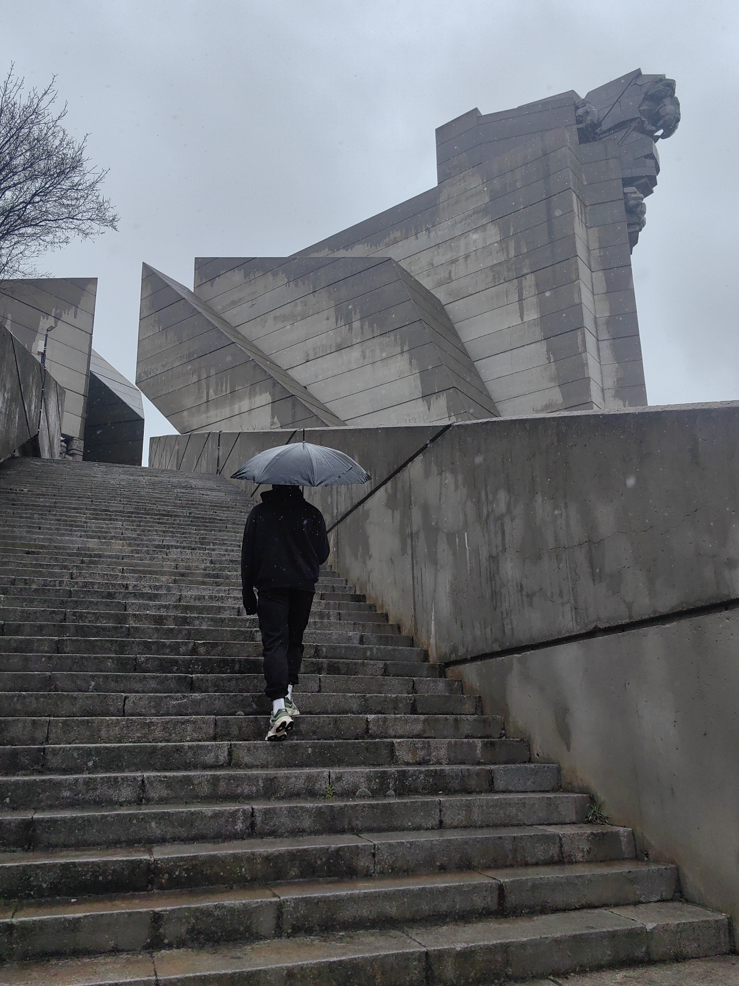Umbrella walker navigates monument steps in rainy Shumen morning