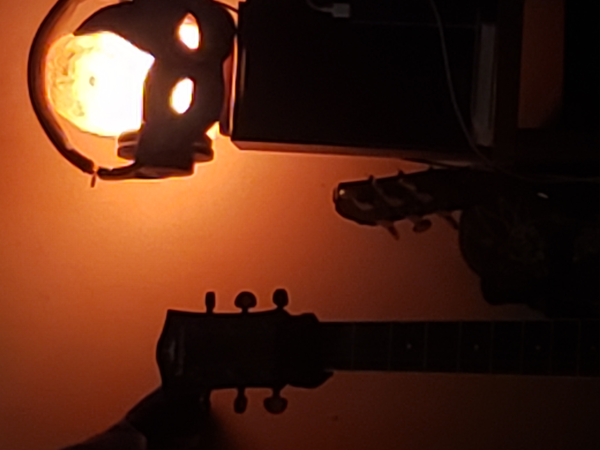 Acoustic guitar and lamp silhouetted against warm orange light