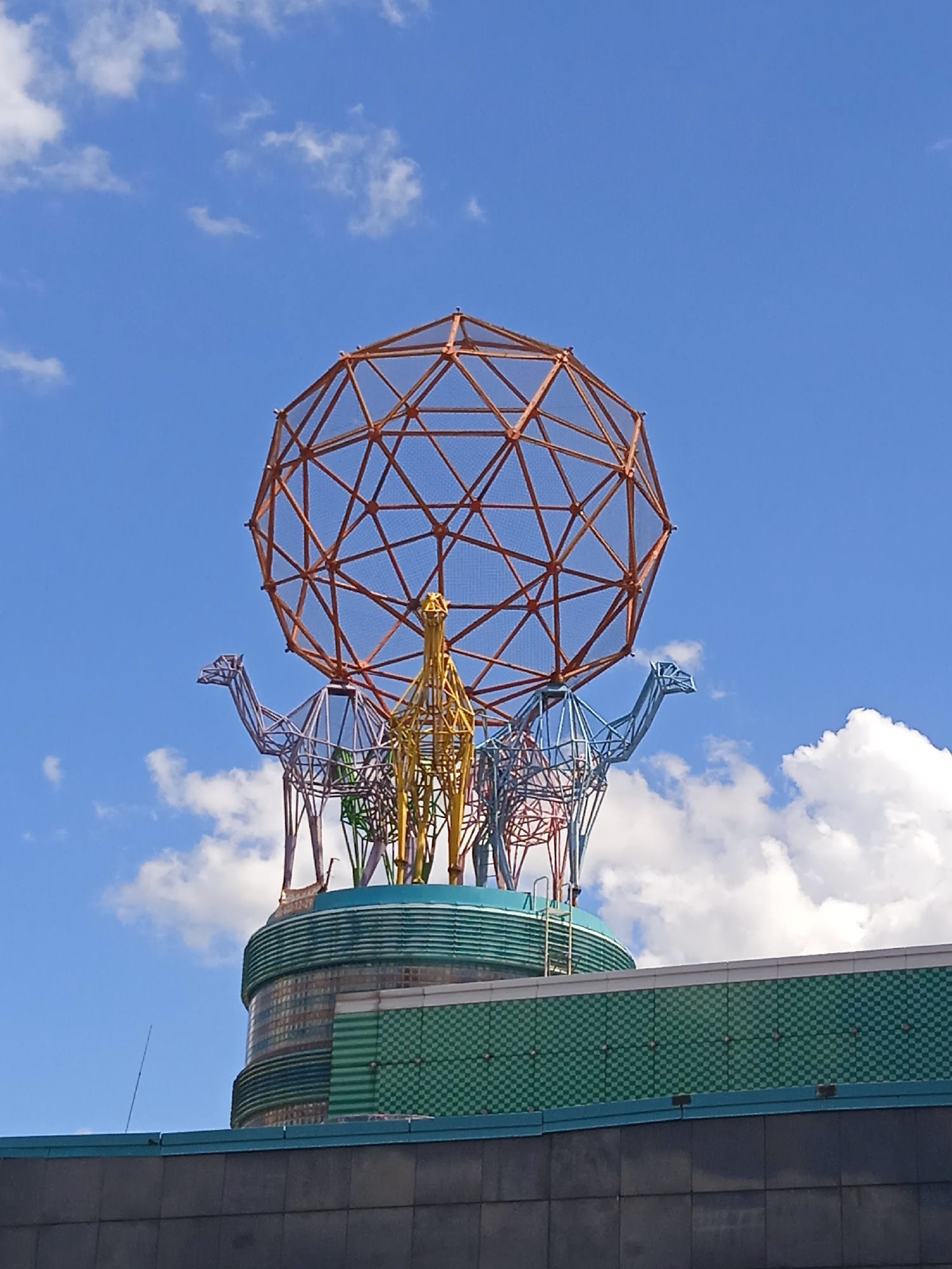 Orange geodesic dome sculpture rises above a city's street gardens