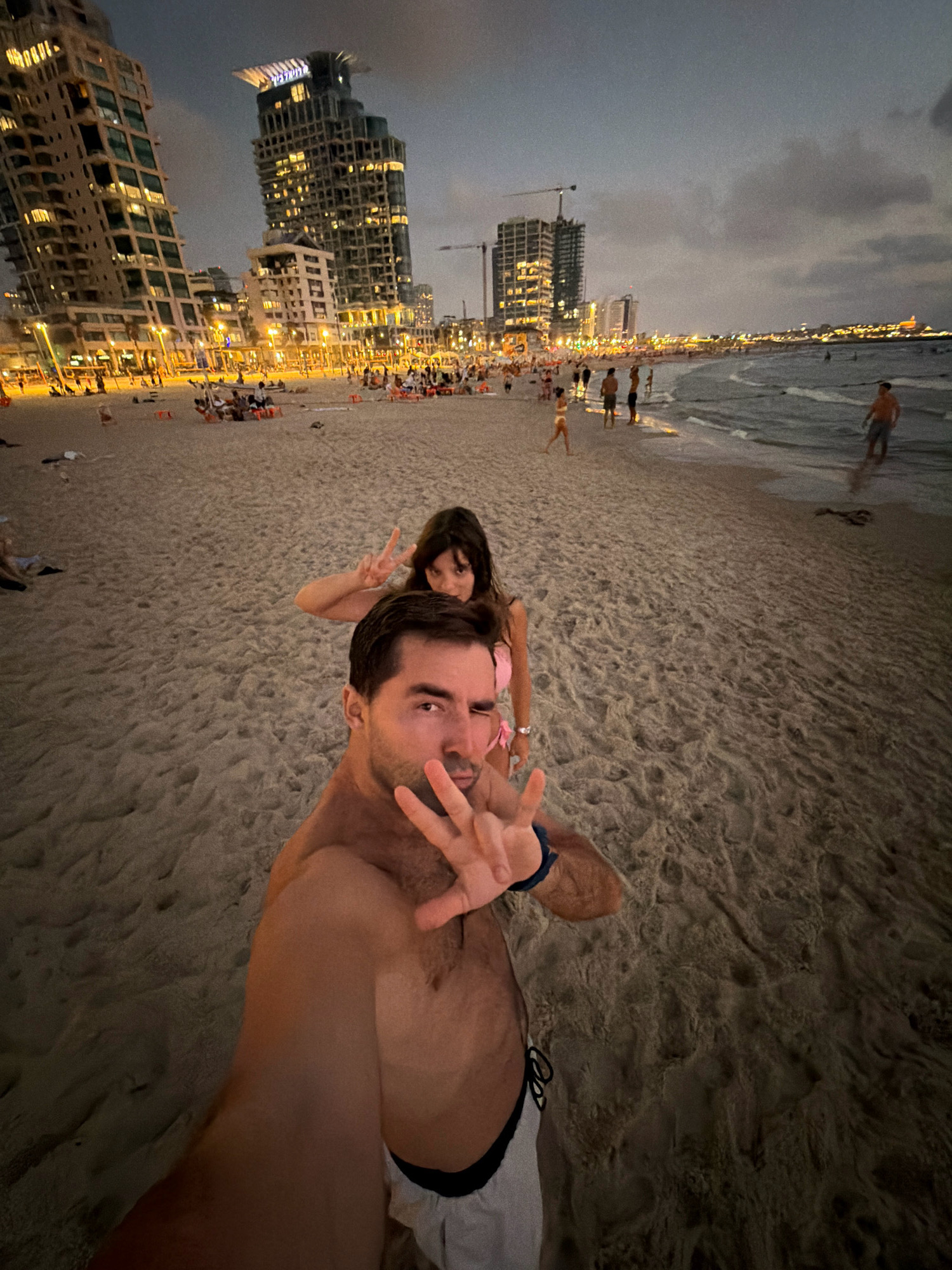 Tel Aviv beach at dusk, skyline towers glowing at twilight.