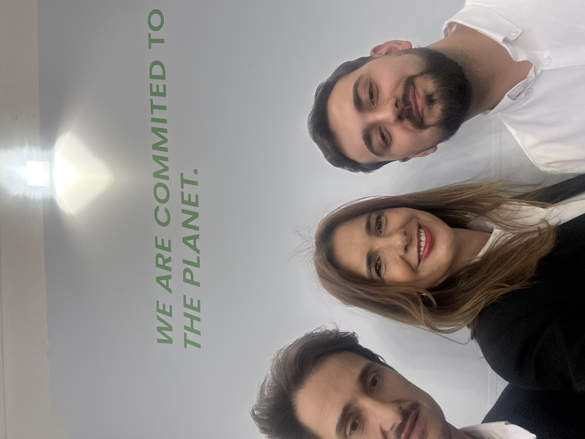 Three people take selfie at environmental message wall in Munich