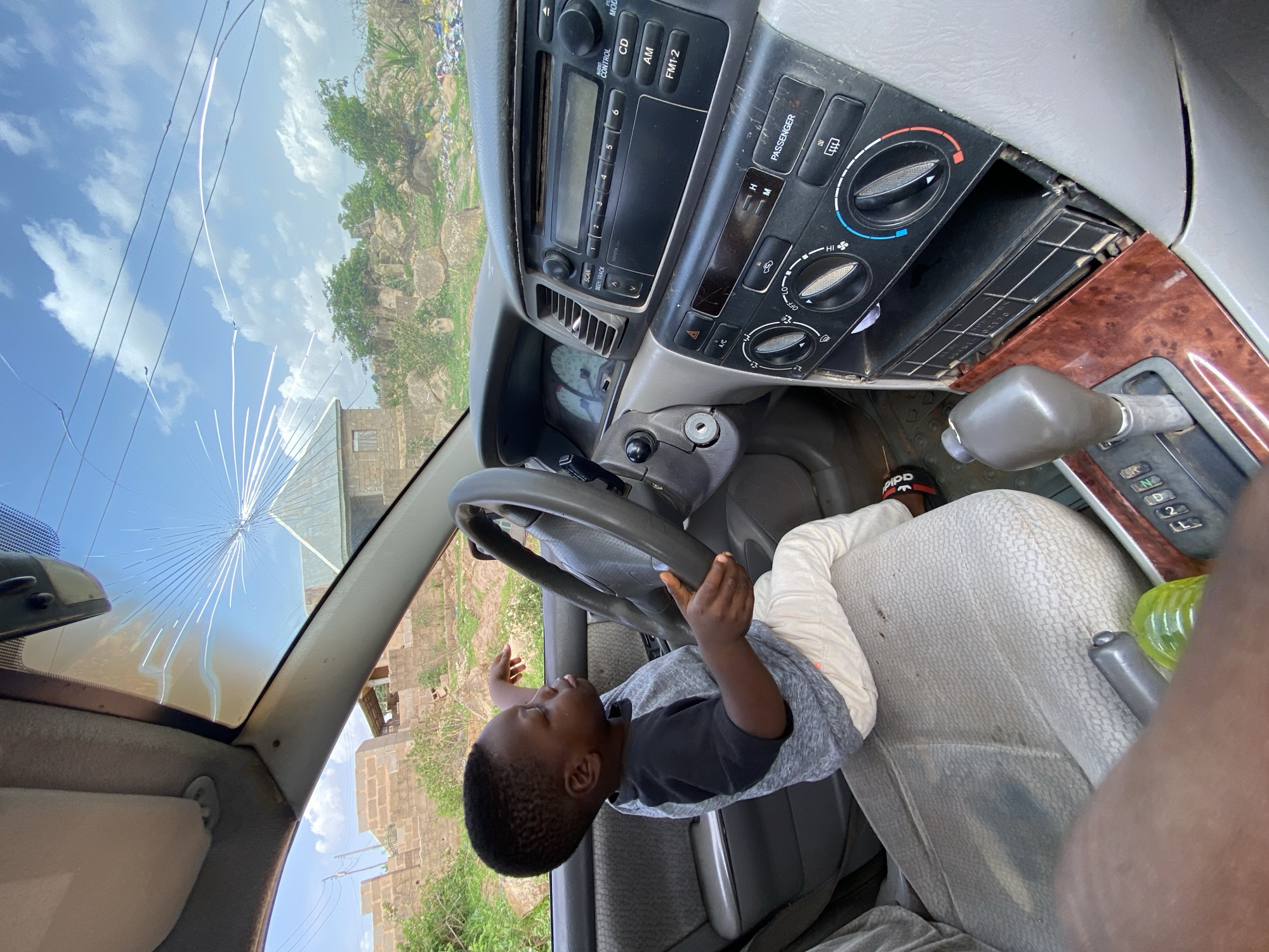 Child plays pretend driving game with parked car in Nigeria