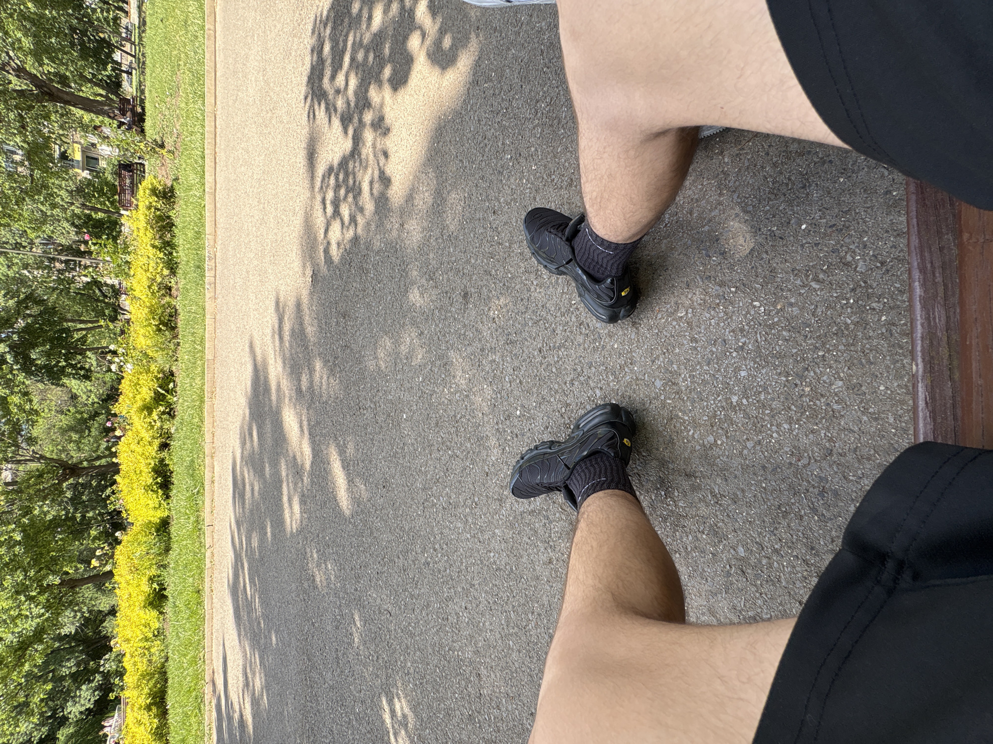Person in athletic wear stands on pavement near greenery