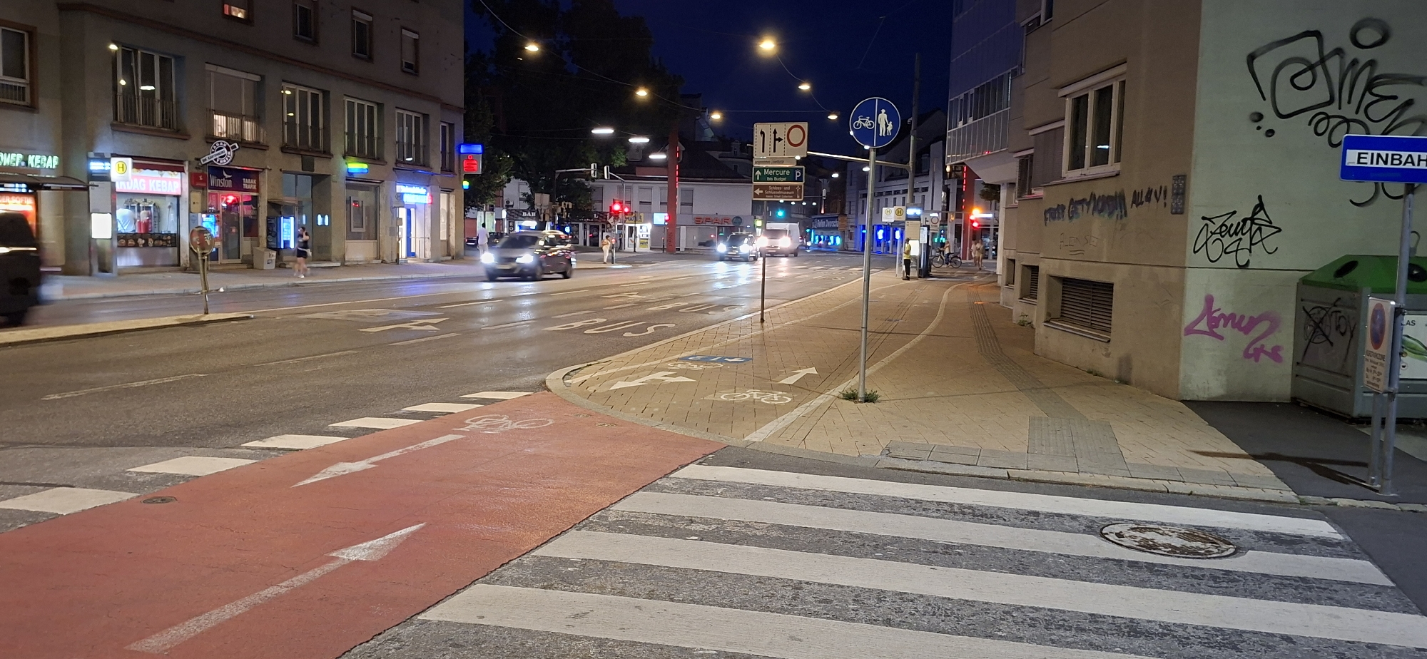 Red bike lane cuts through a quiet city street at night