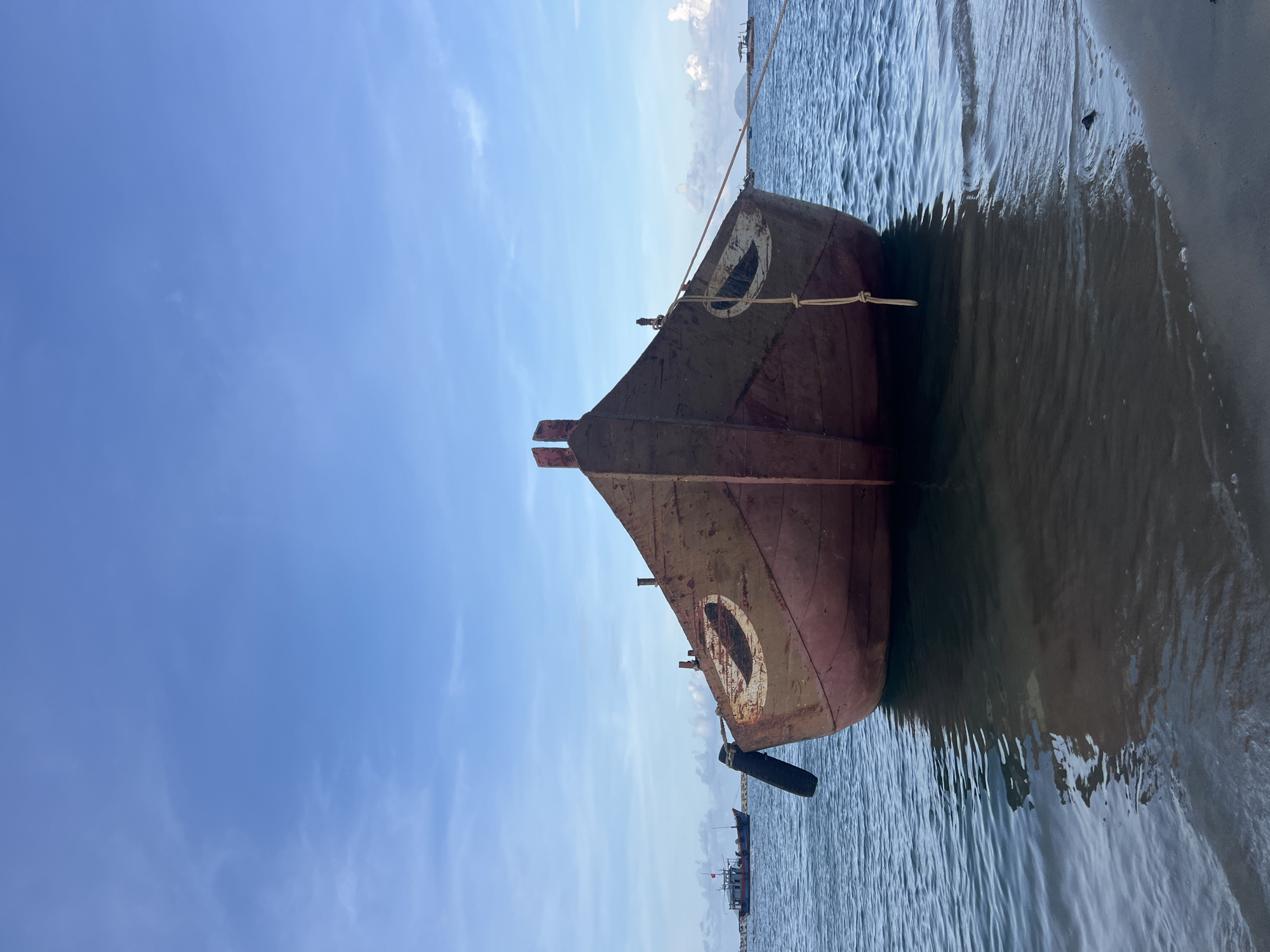 Worn red fishing boat moored in Hoi An's shallow coastal waters