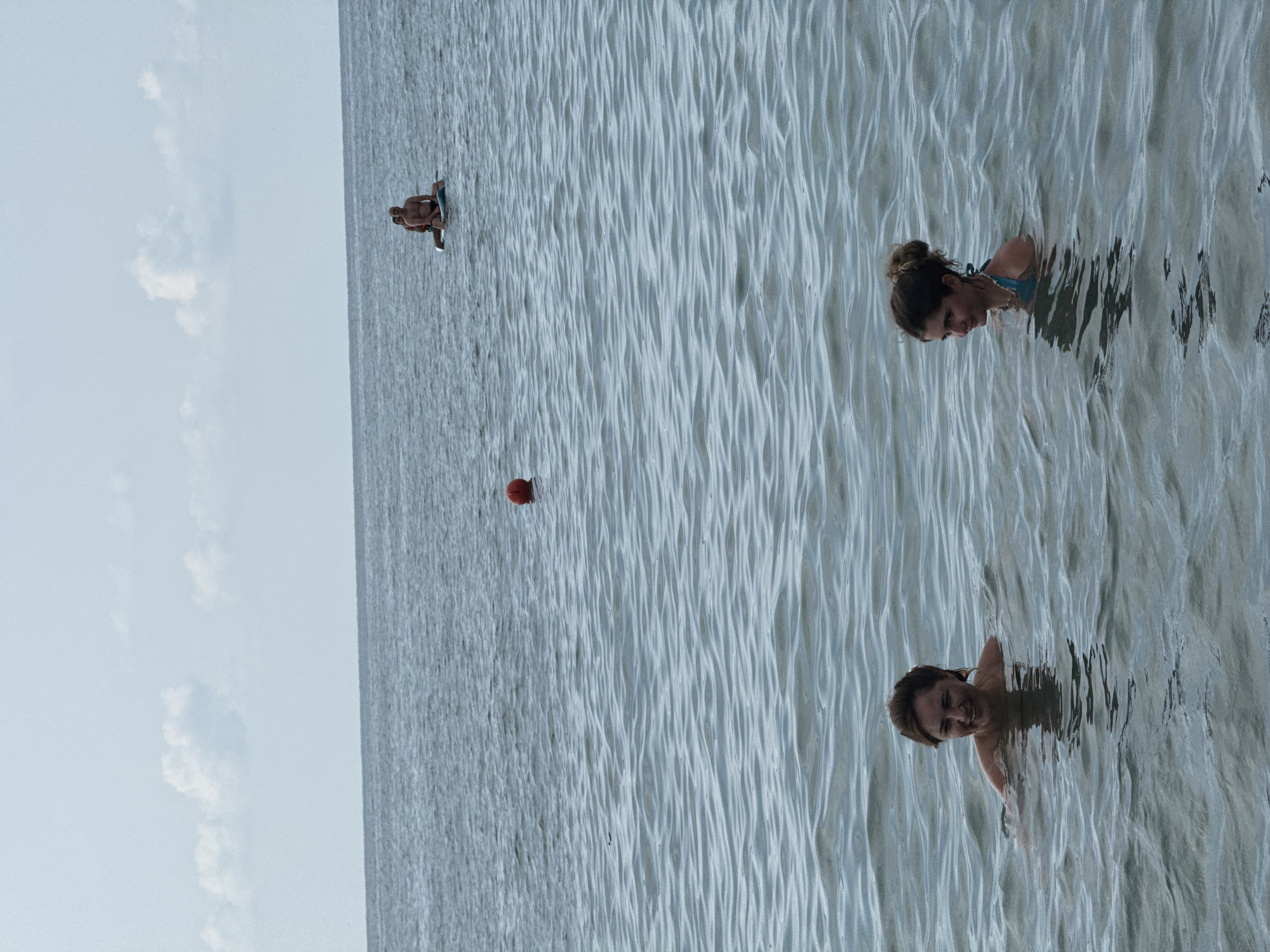 Crowded pebble beach, overcast skies, swimmers in choppy water.