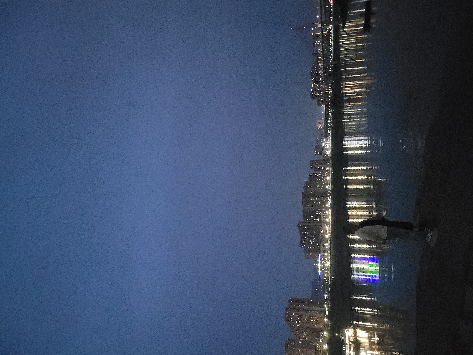 Individual stands by water viewing city lights in Shapingba