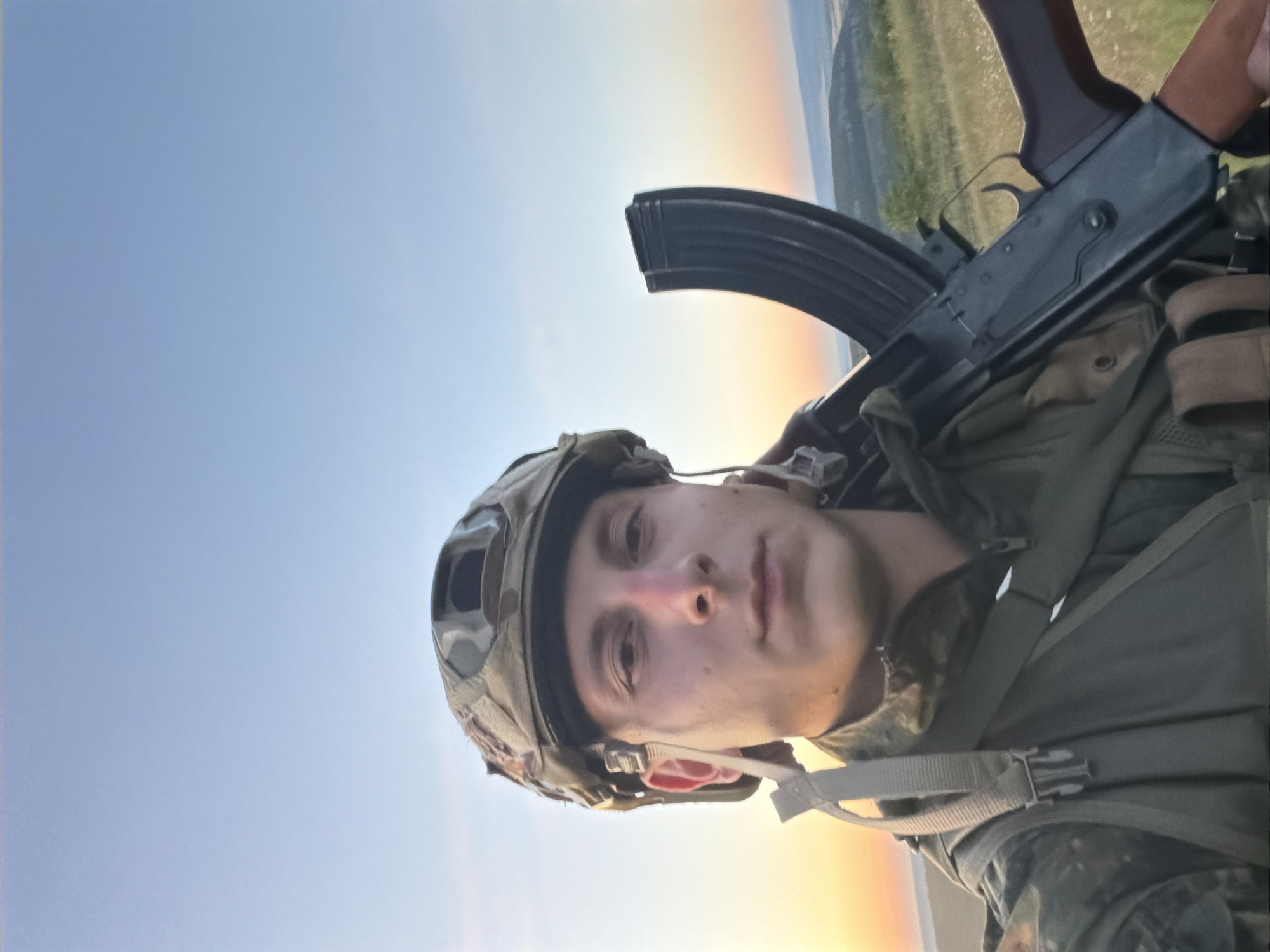 Military gear and AK-47 photographed outdoors at sunset