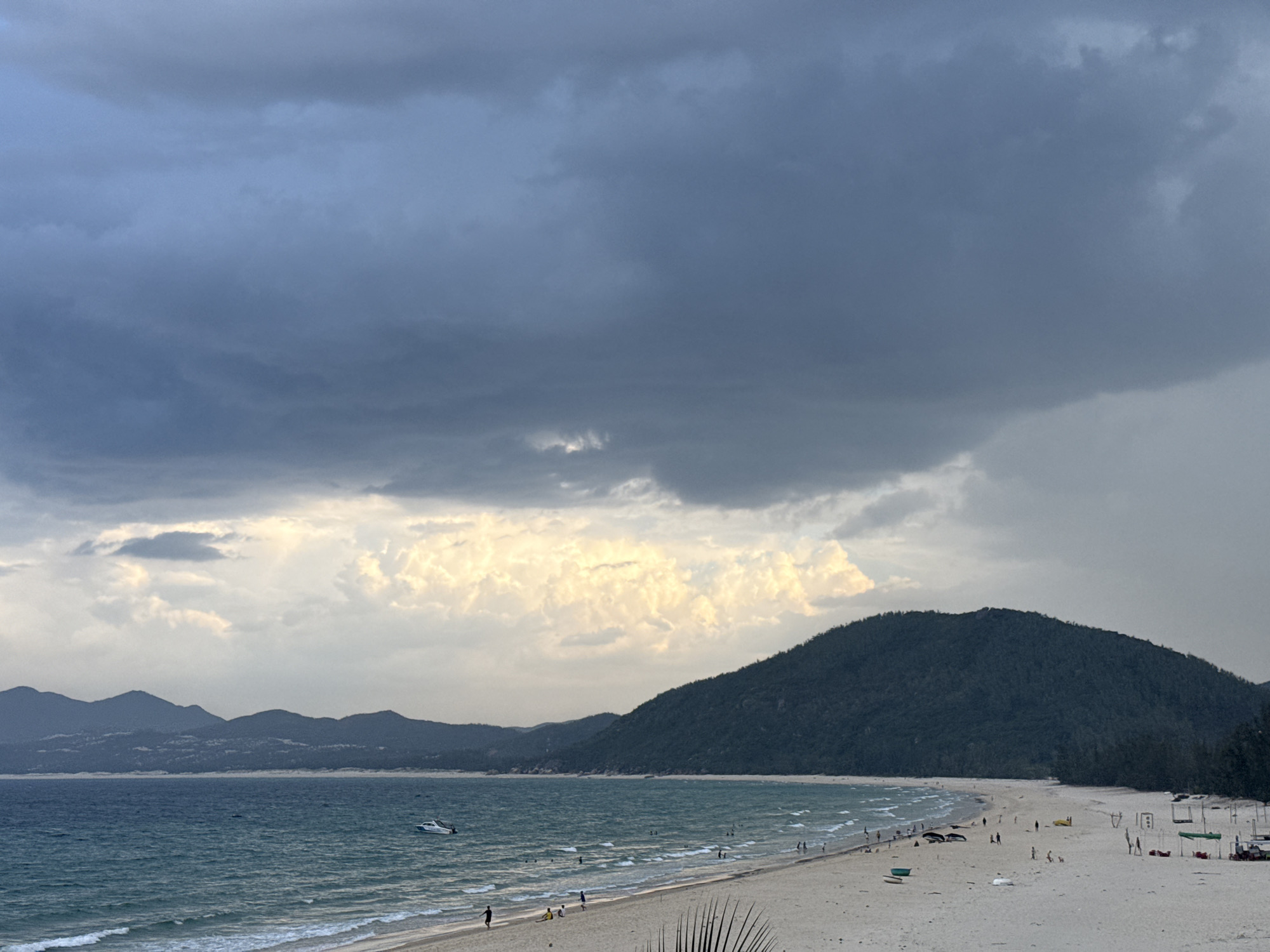 Stormy skies over a turquoise beach with scattered visitors