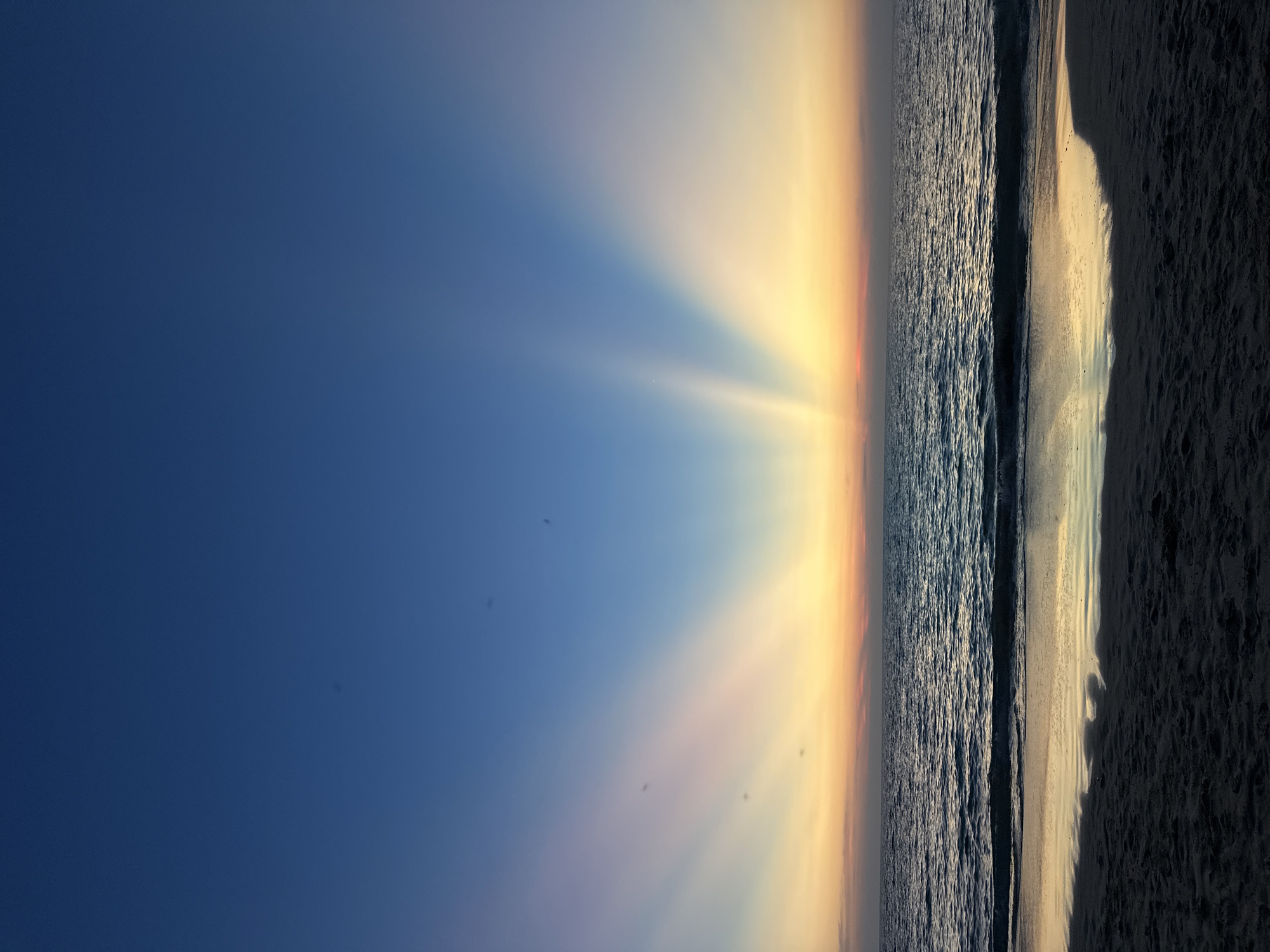 Woman photographs dramatic sunset with crepuscular rays at Thai beach