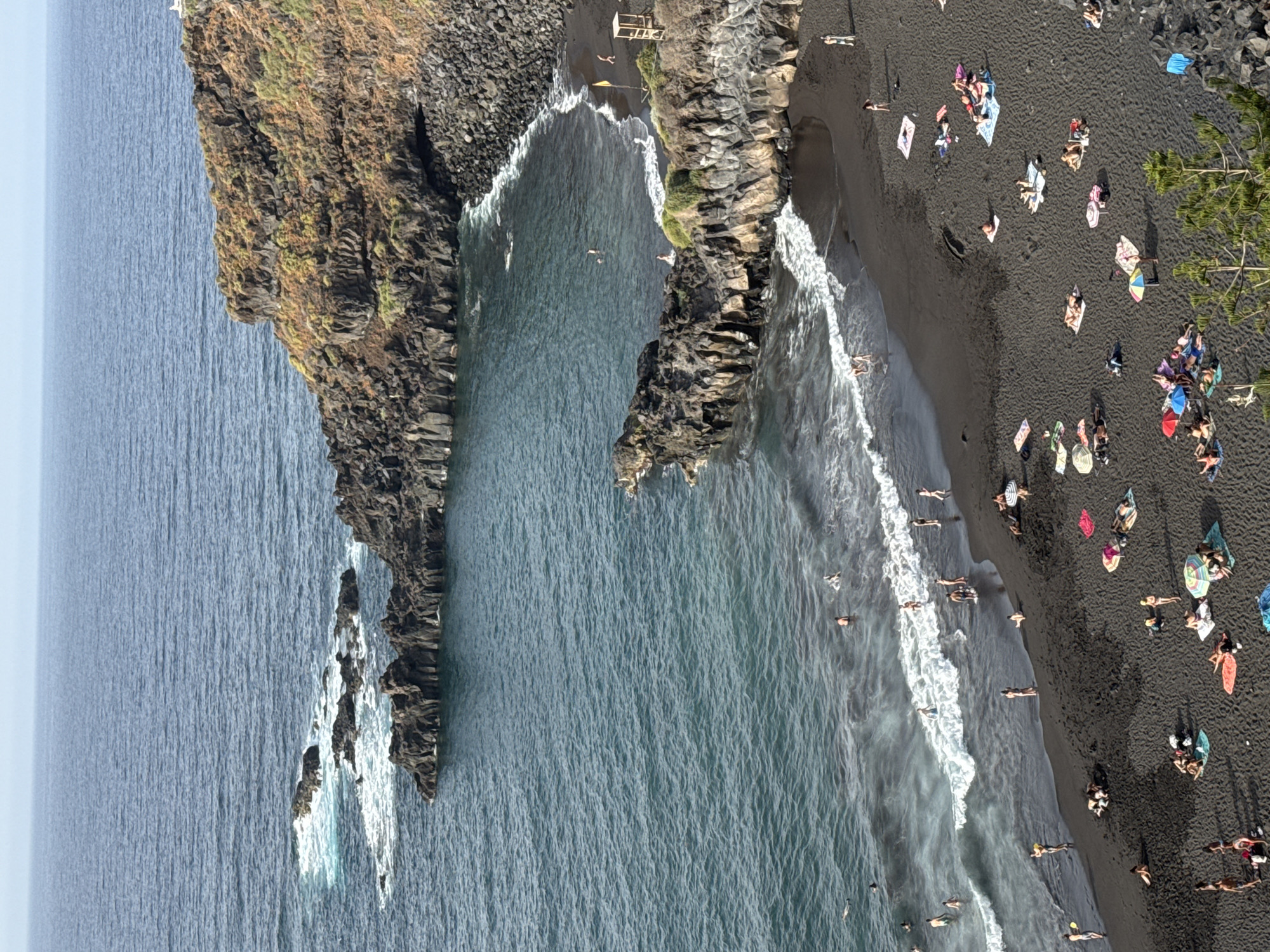 Busy black sand beach, aerial and cliff views