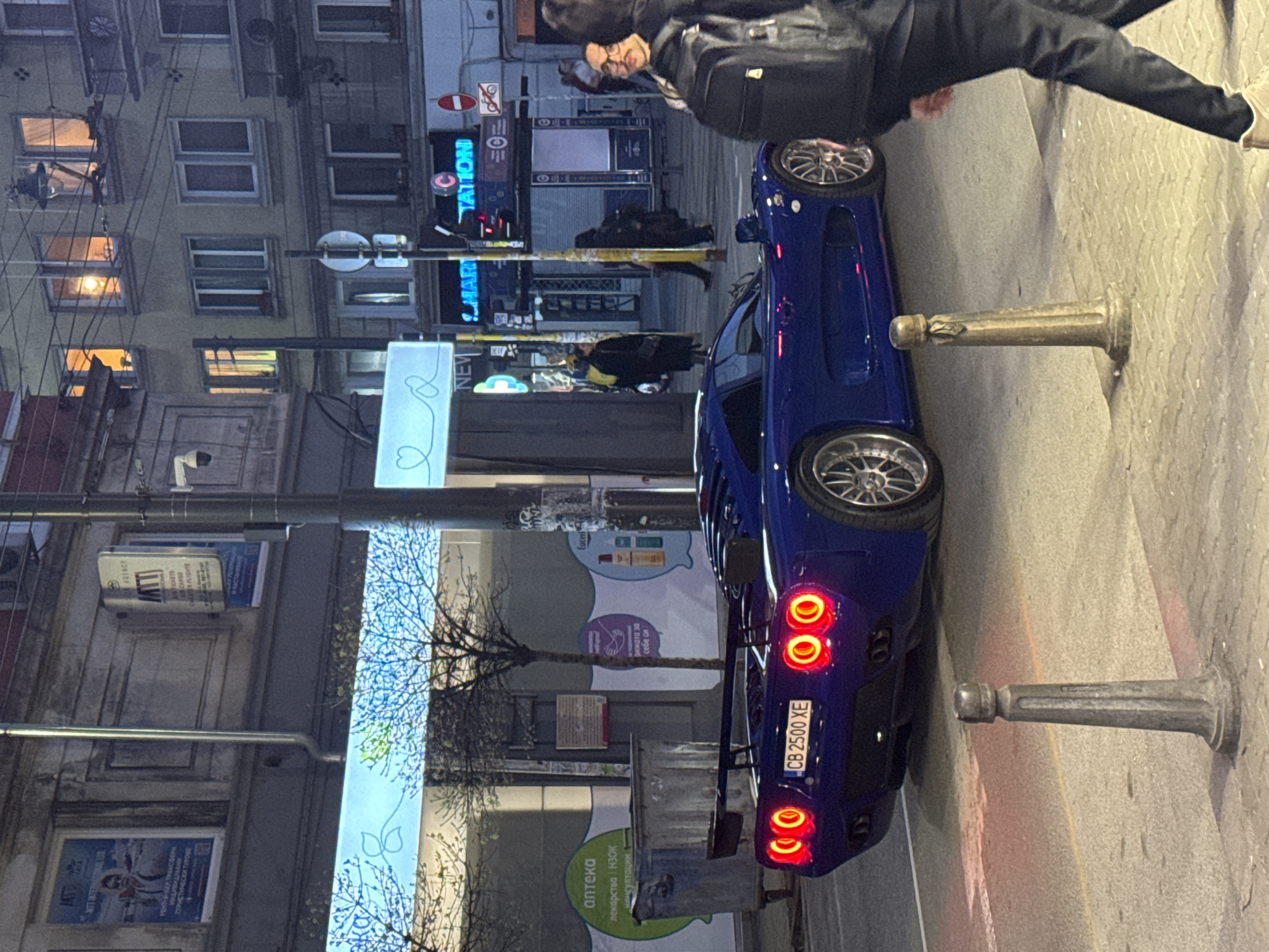 Blue sports car parks on Sofia sidewalk, person observed nearby