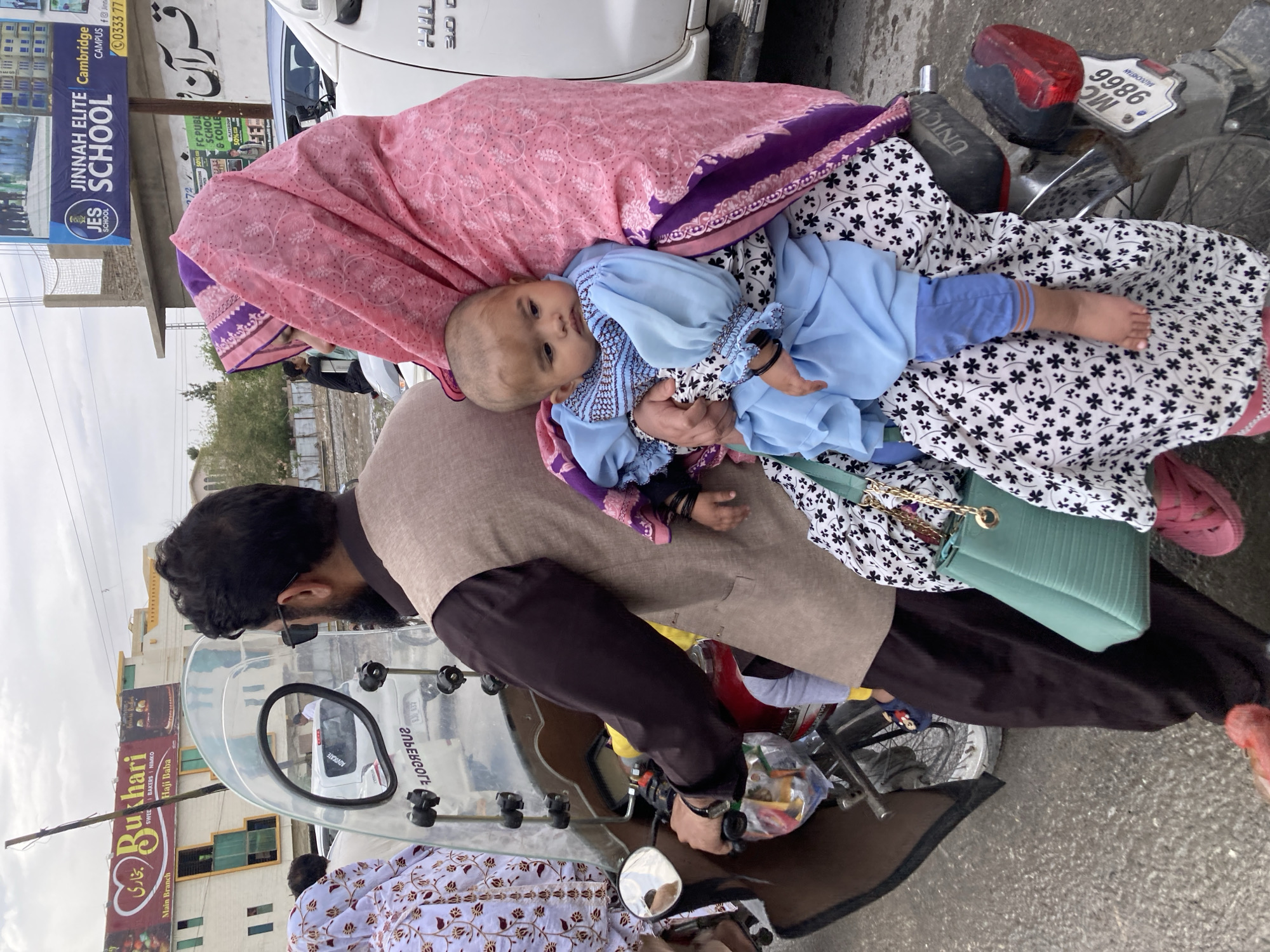 Family travels by motorcycle through Quetta streets under overcast sky