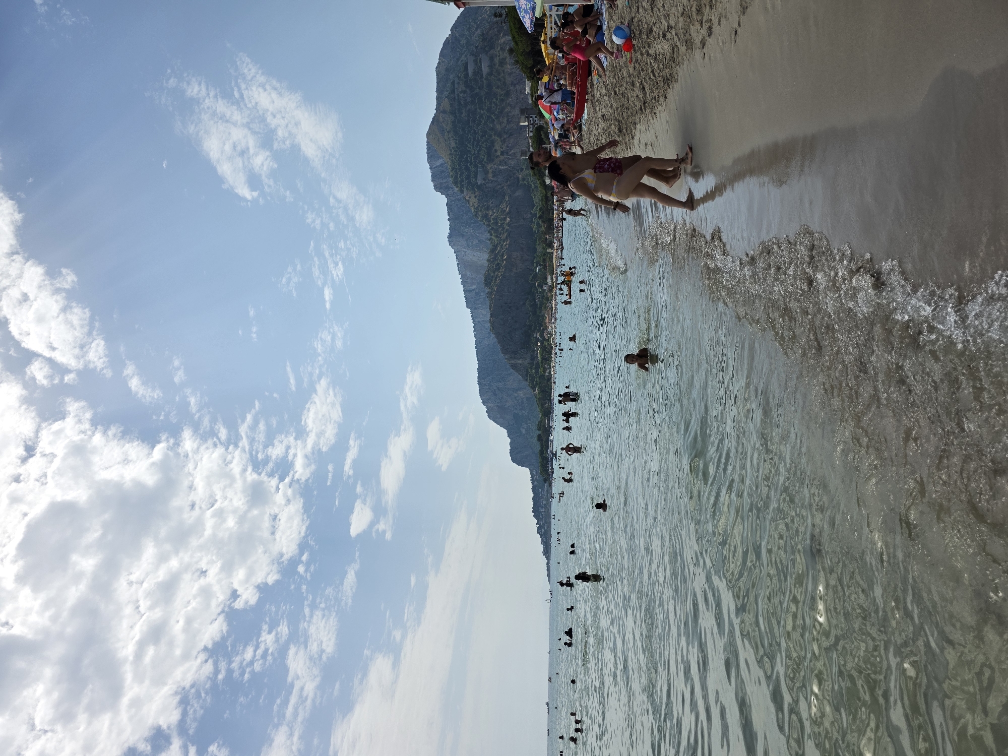 Crowded beach day with calm water and a mountain backdrop