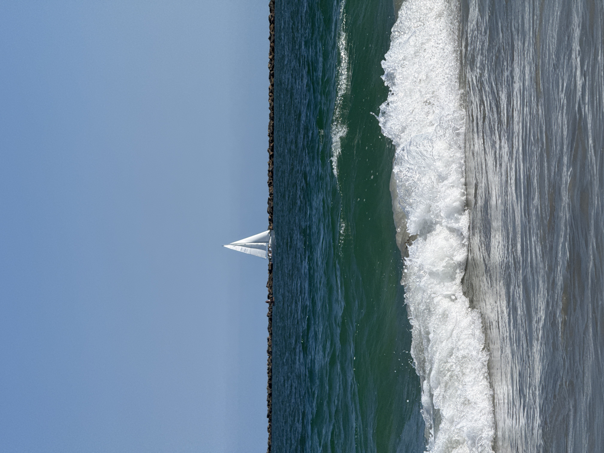 Sailboat cruising past Wrightsville Beach breakwater on calm day