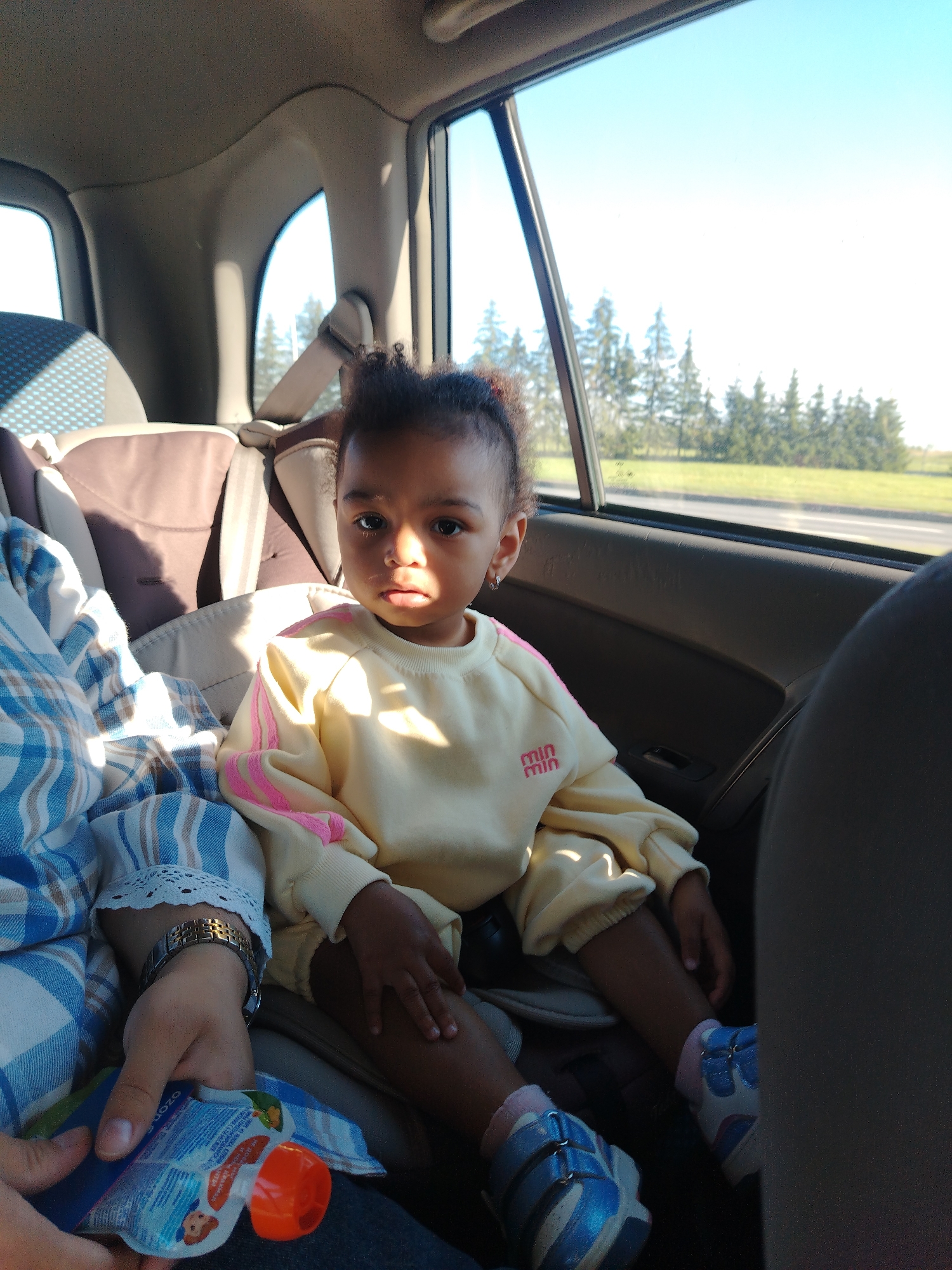 Child in yellow sweatshirt seated in the back of a car