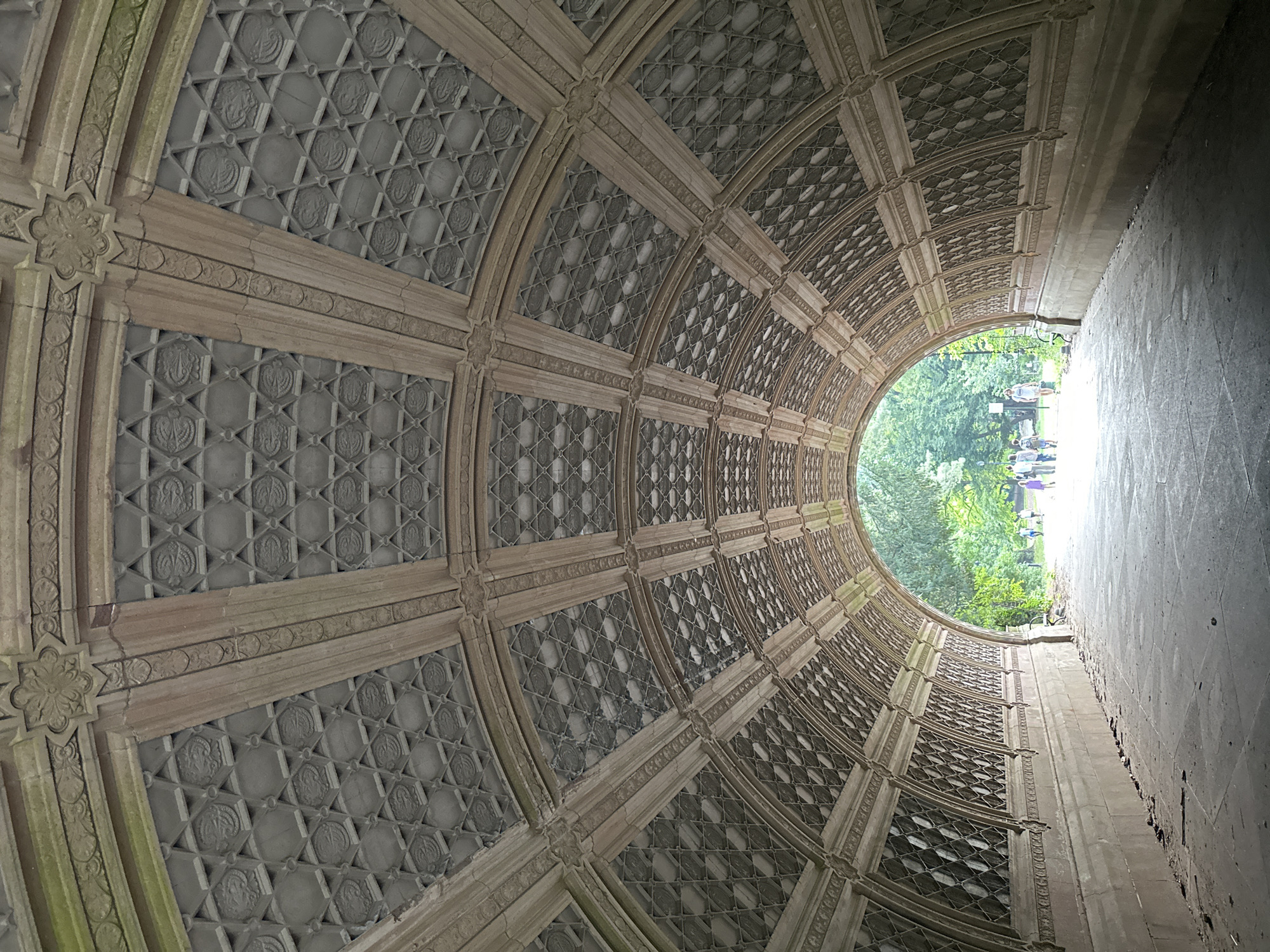 Looking through a decorative stone tunnel into a sunlit park path