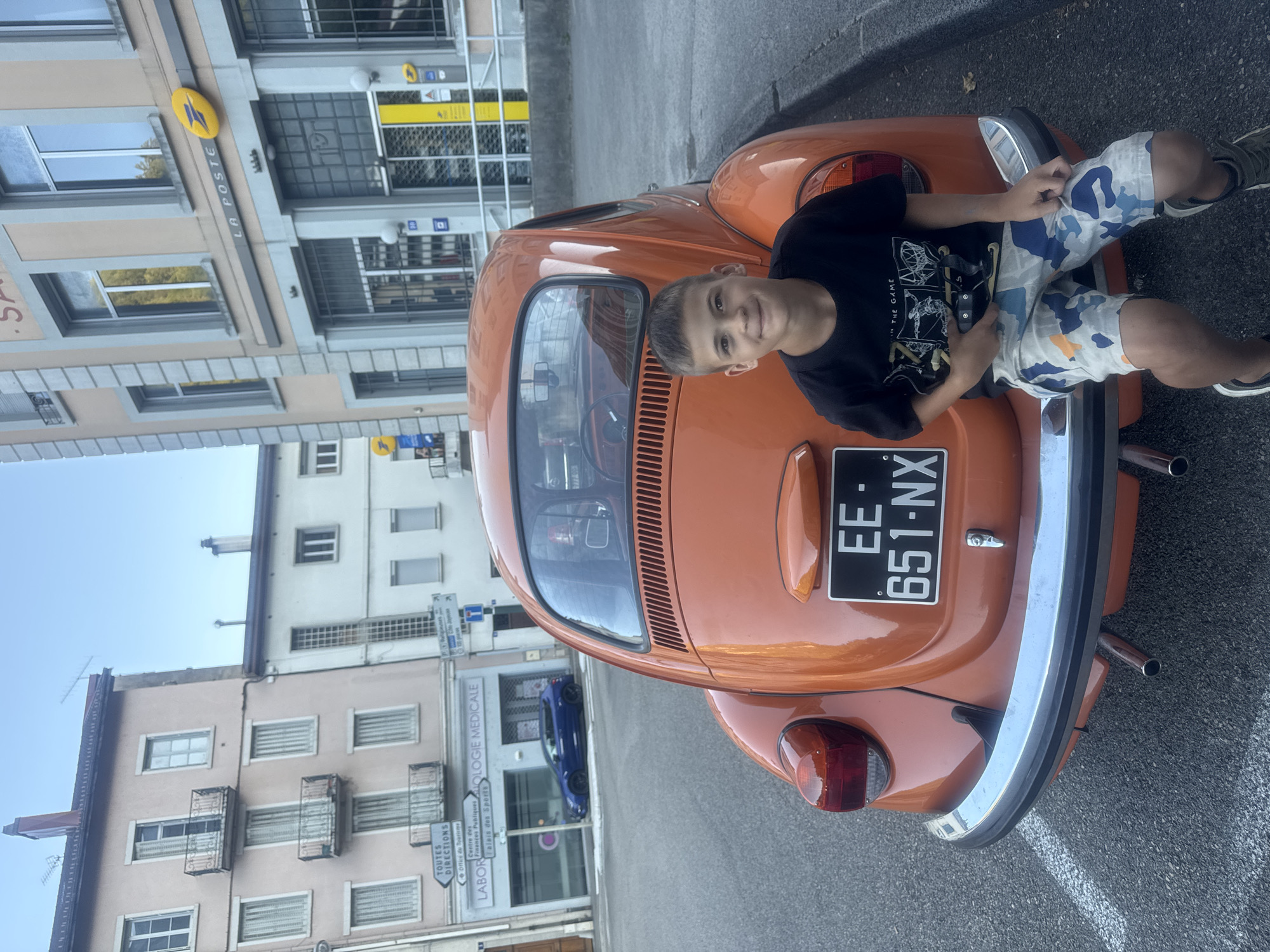 Afternoon street scene in Saint-Claude with an orange Beetle and a balance bike.
