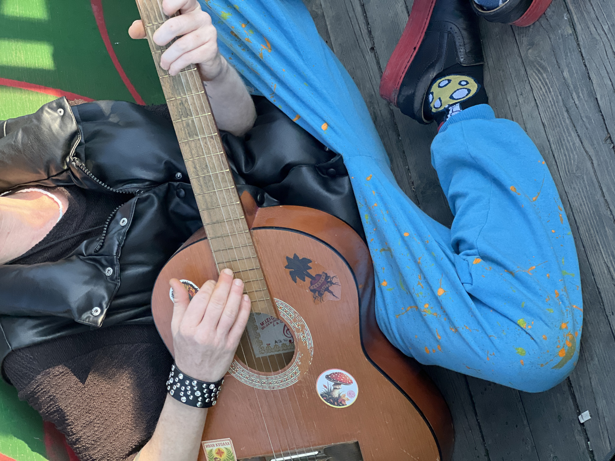 Street musician plays guitar on Belgrade deck wearing paint-splattered pants