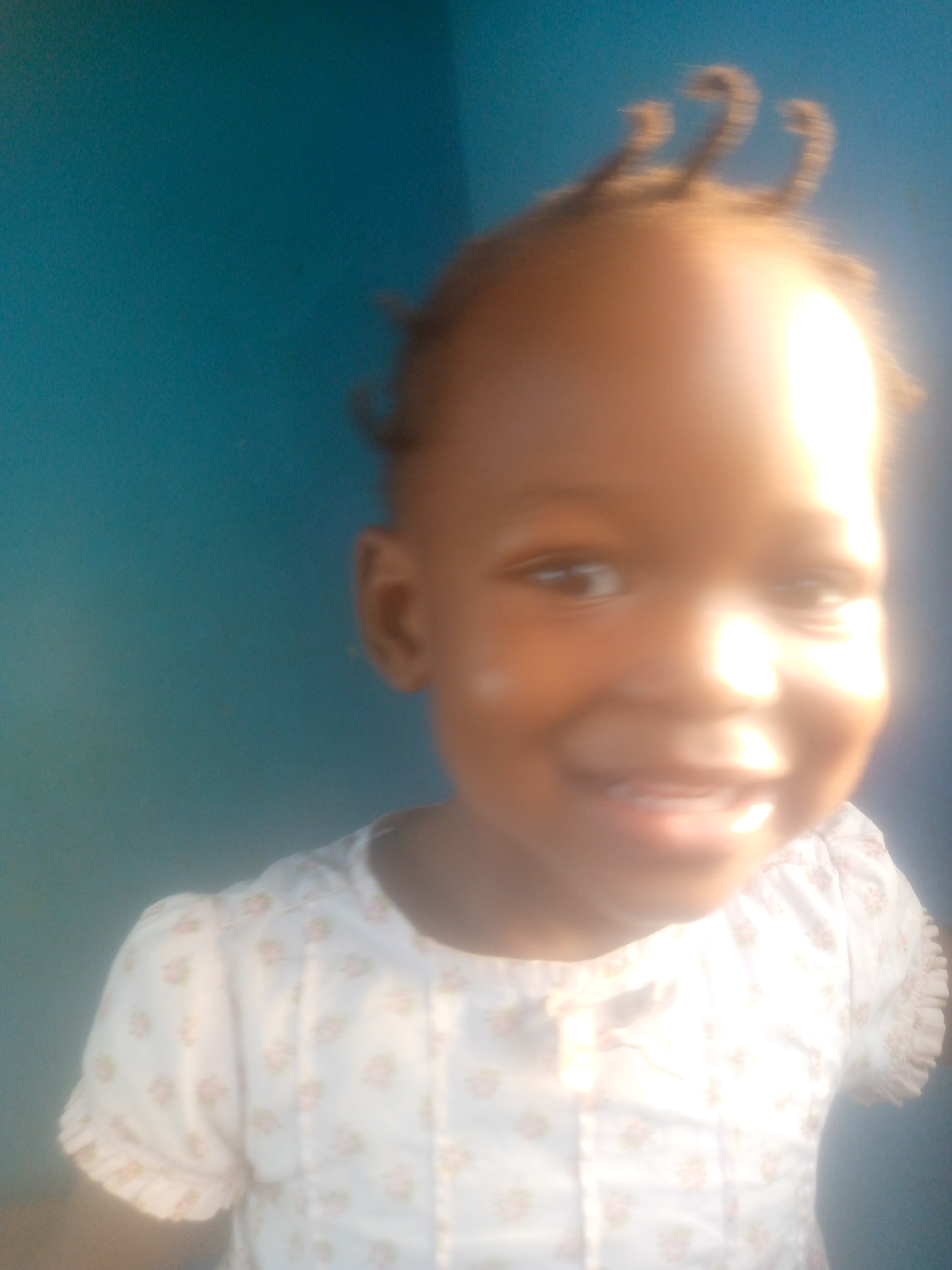 Child photographed smiling in floral shirt against colored wall