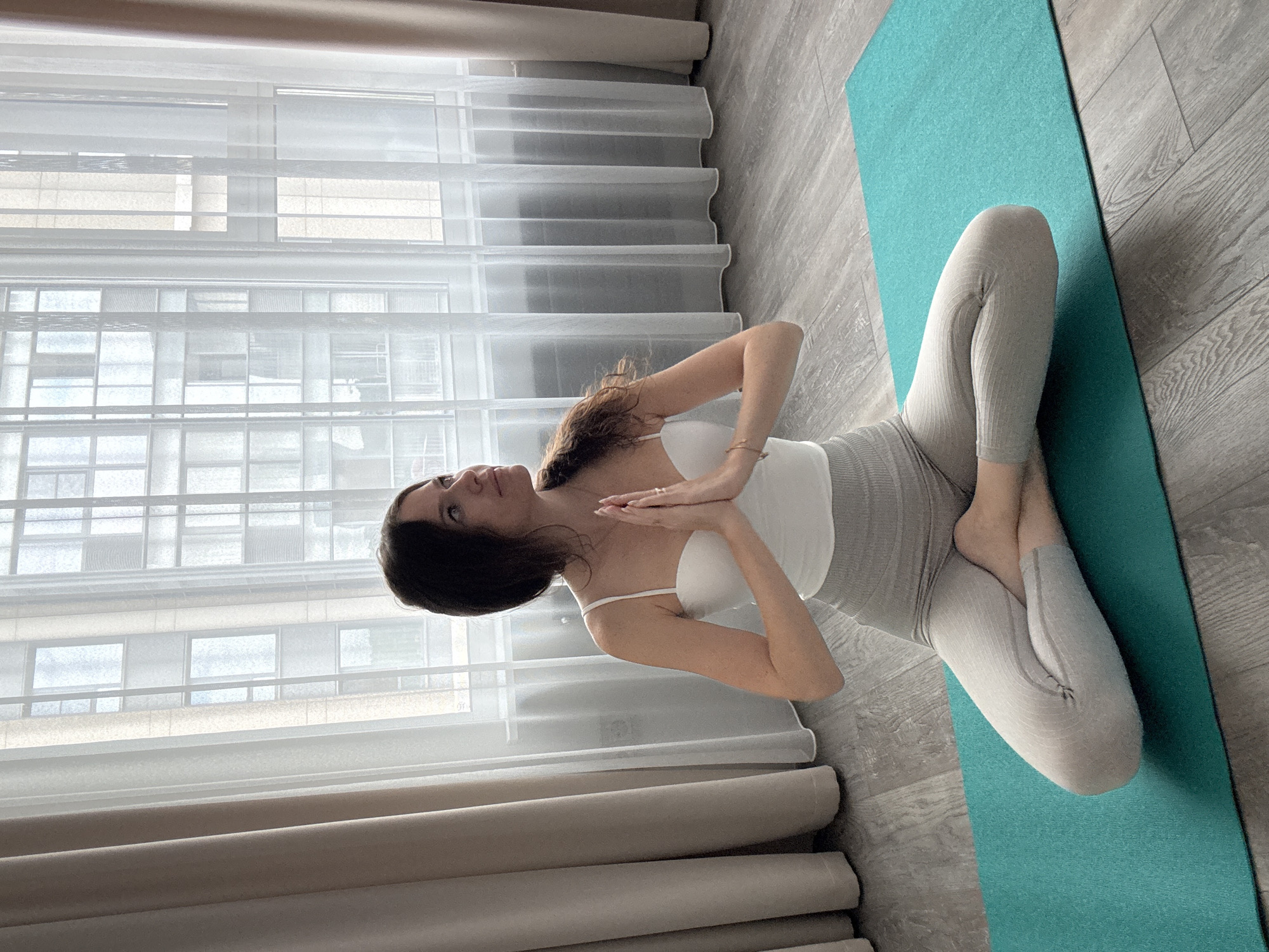 Quiet meditation pose on a teal mat in a wood-floored room