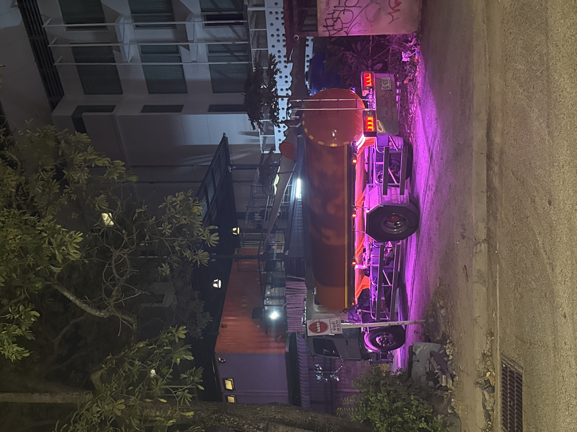 Neon-lit tanker truck parked on a Ko Samui dirt road at night