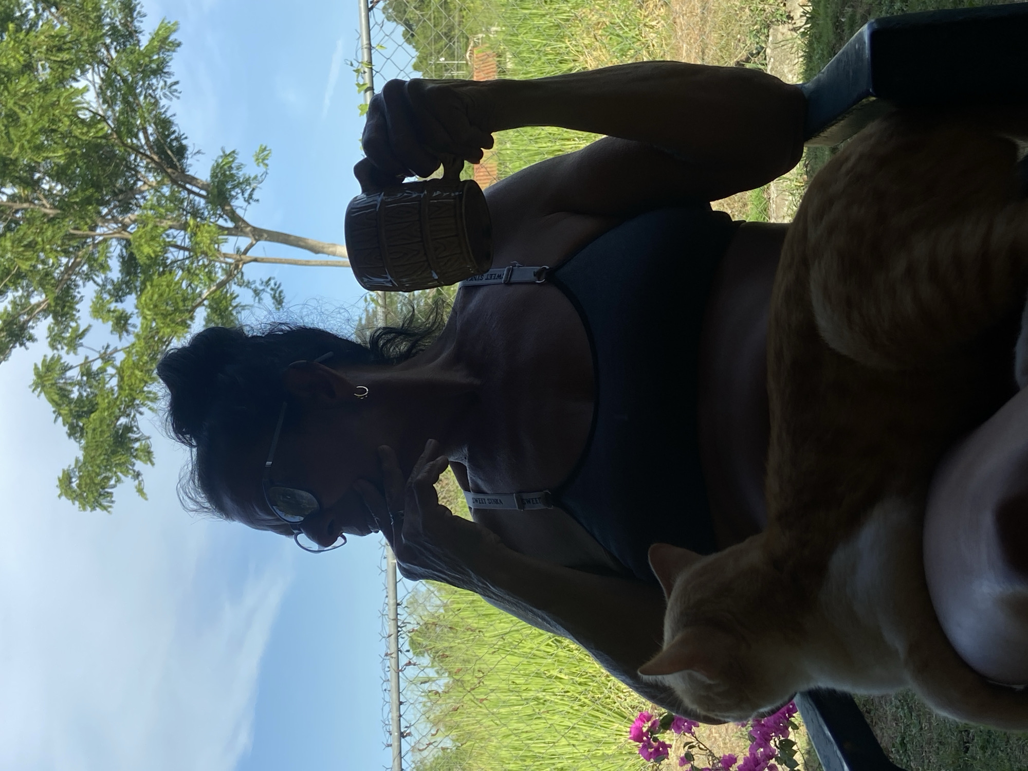 Woman with mug sits in garden with orange cat
