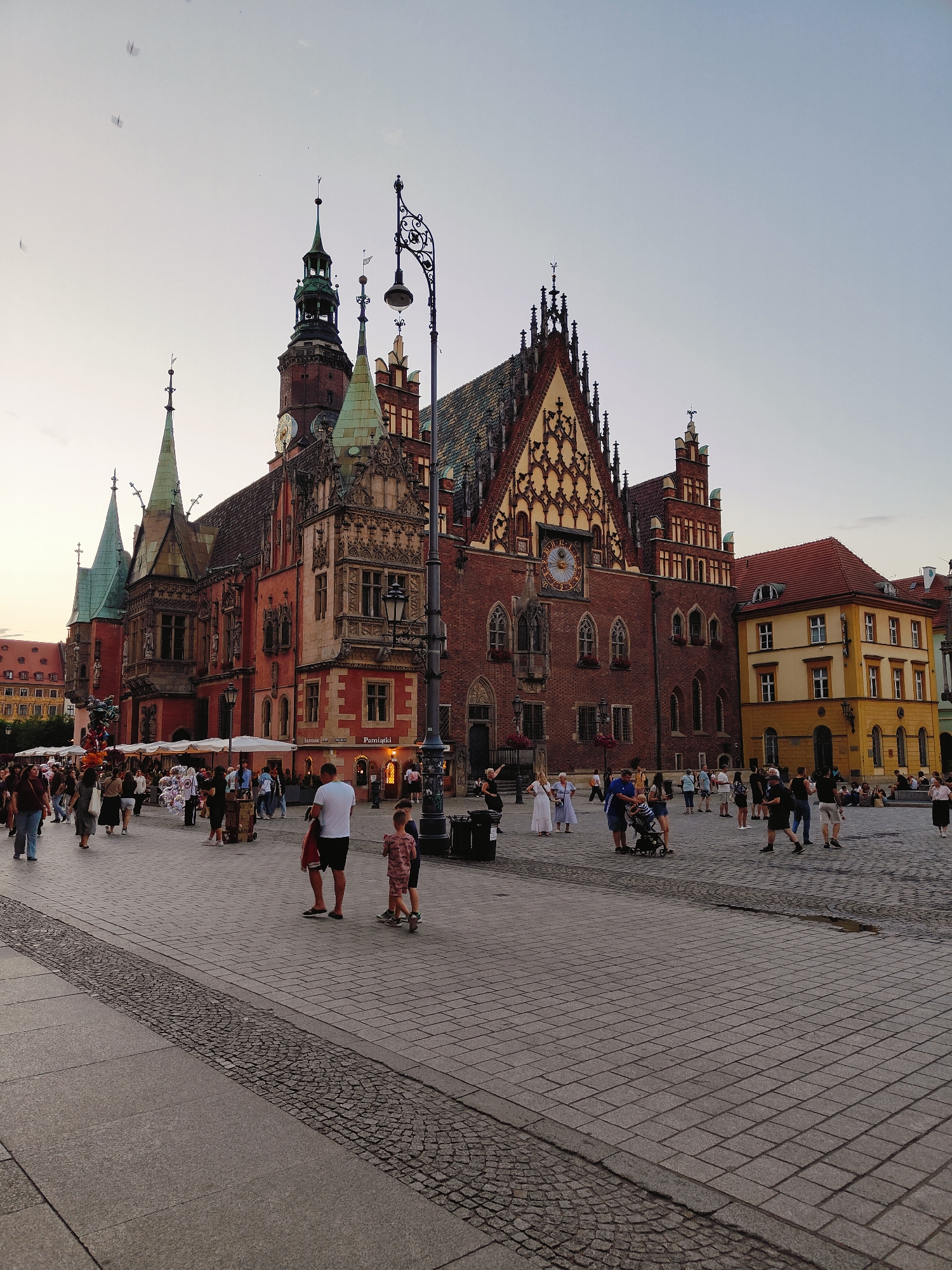 Busy European Gothic town square with clock tower, midday activity
