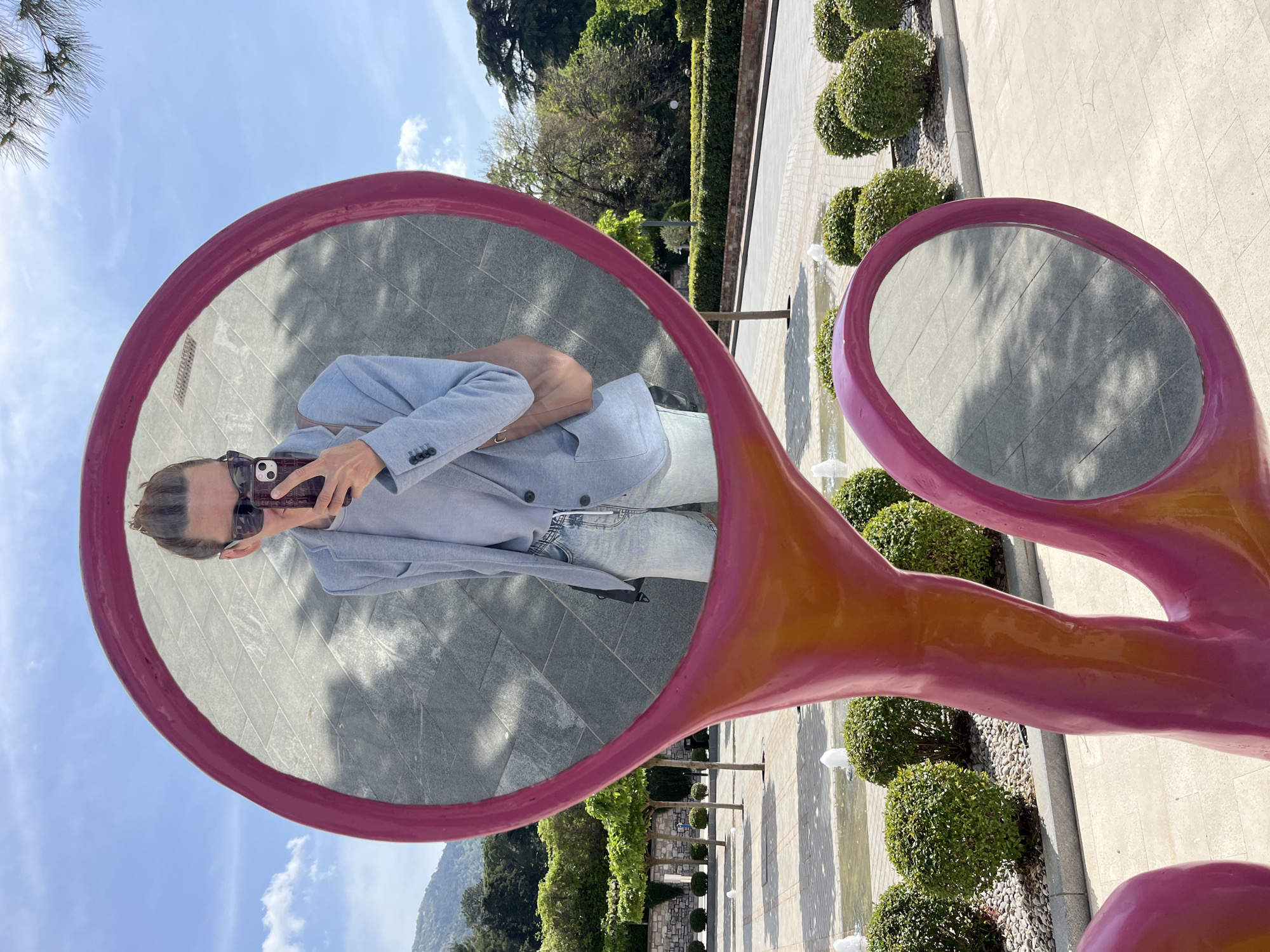 Tourist poses in pink mirror scissors sculpture in Tivat