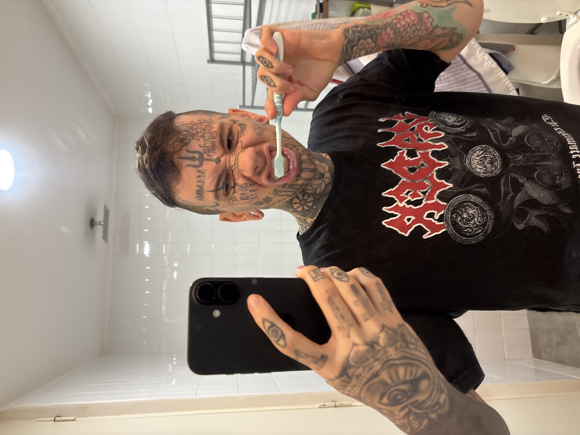Tattooed person takes bathroom selfie while brushing teeth