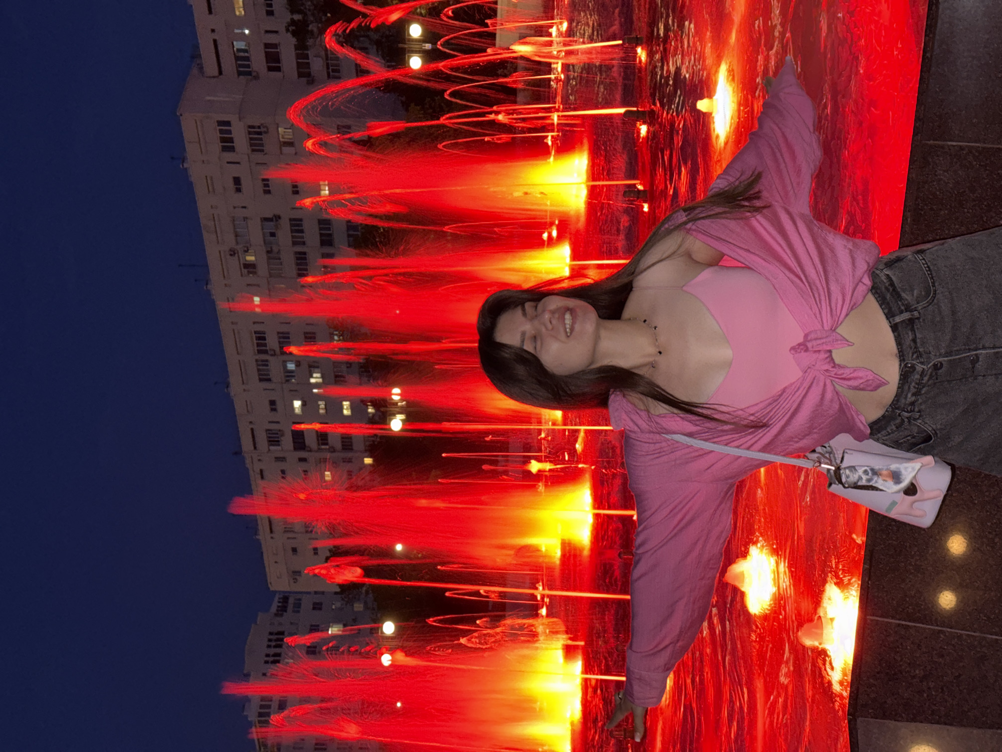Woman poses at illuminated fountain during evening park visit