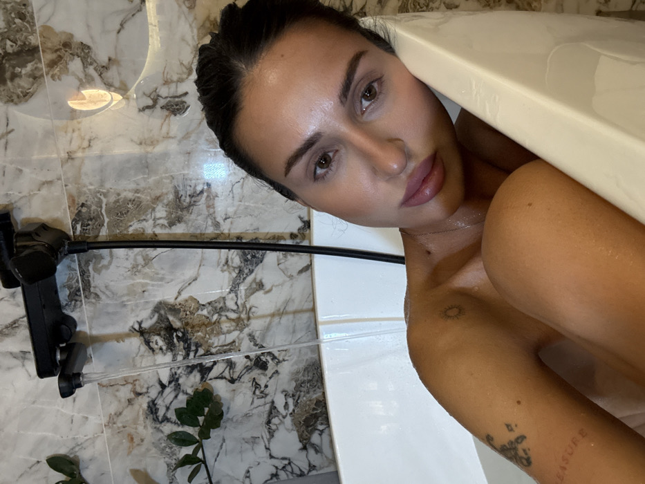 Woman photographed in bathroom with modern fixtures, tattoos visible