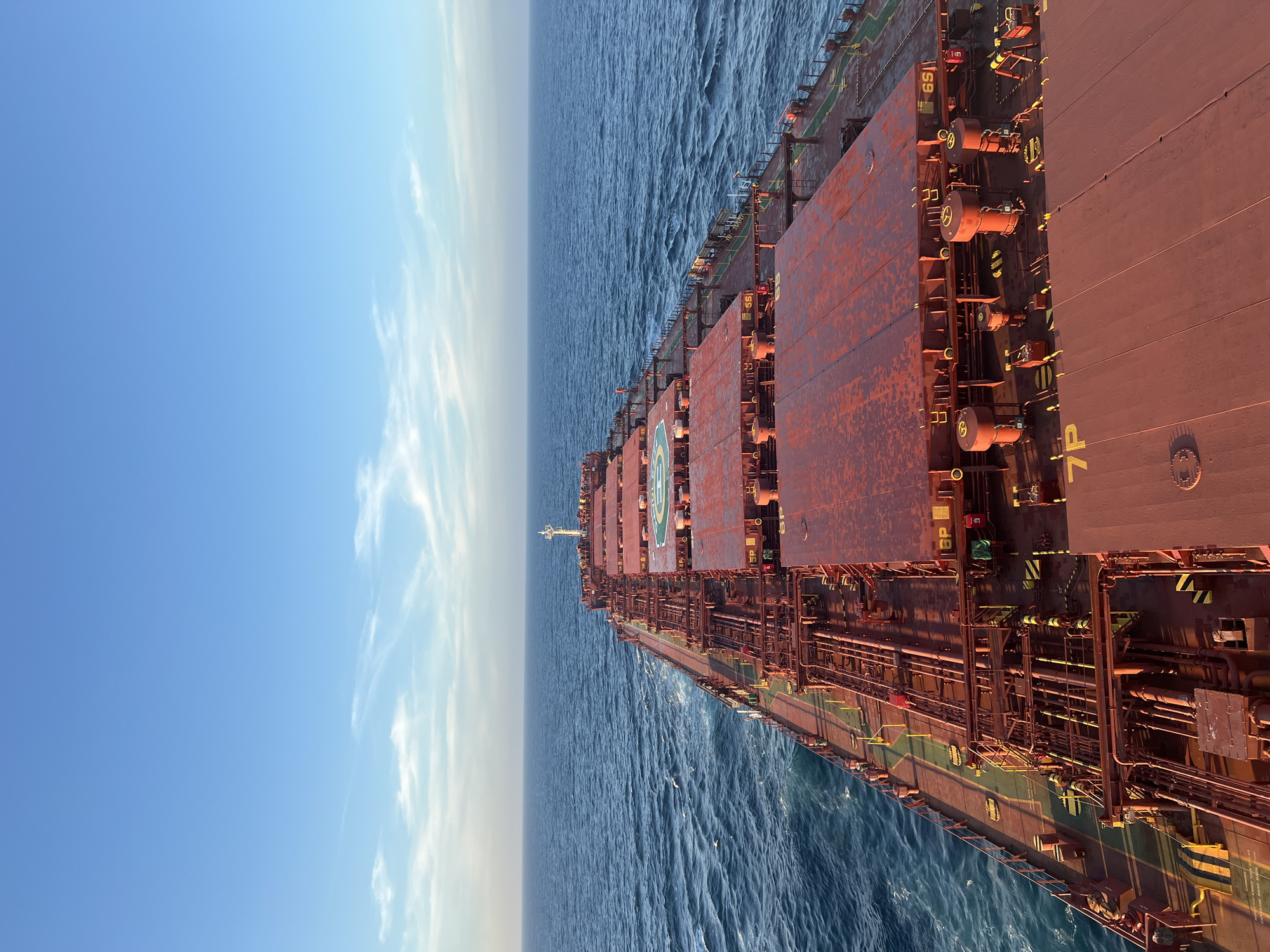 Red cargo ship crosses open ocean through a shifting day